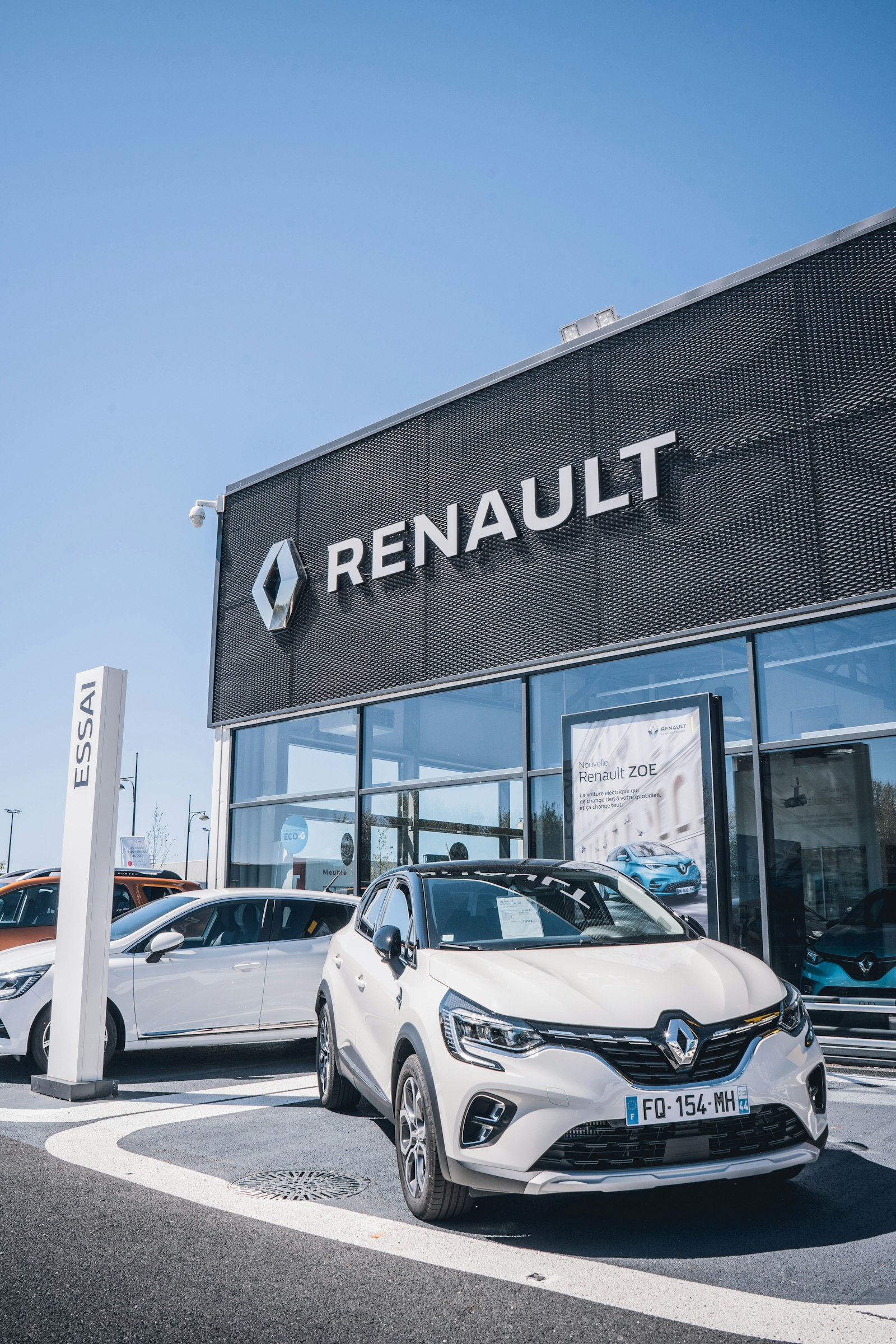 Coche compacto blanco Renault aparcado frente a concesionario europeo con cielo azul despejado