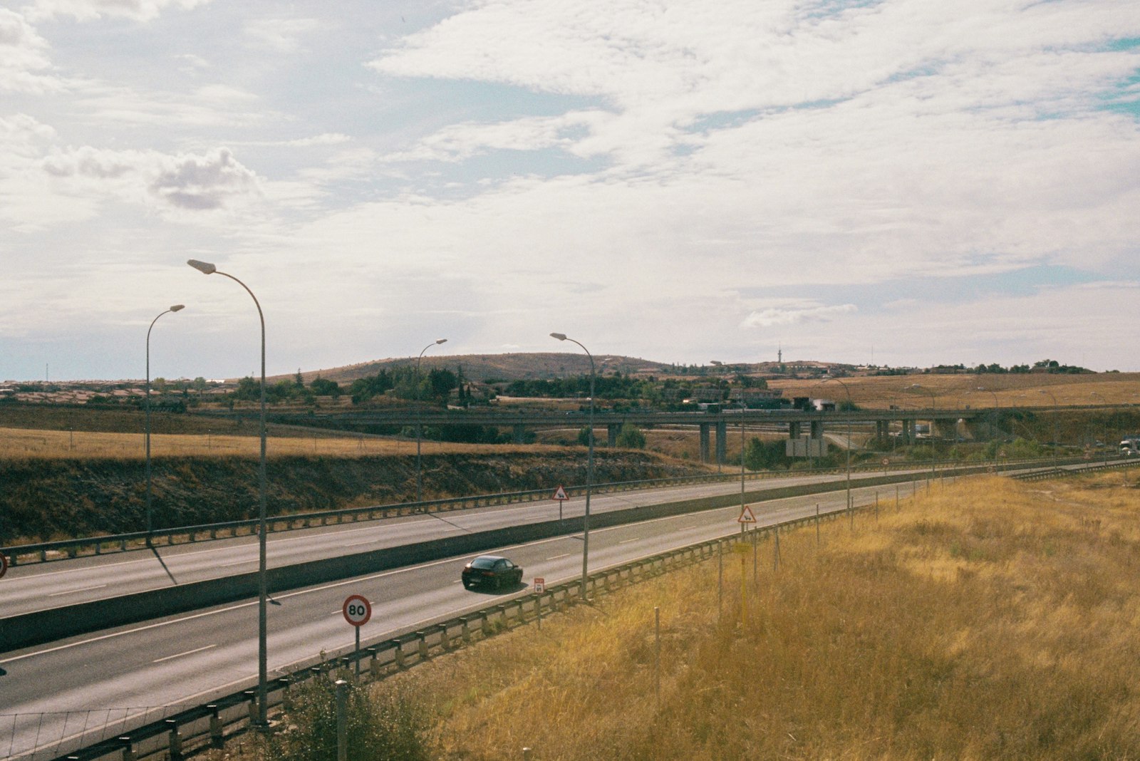Car driving on Spanish motorway through dry golden hills with speed limit sign