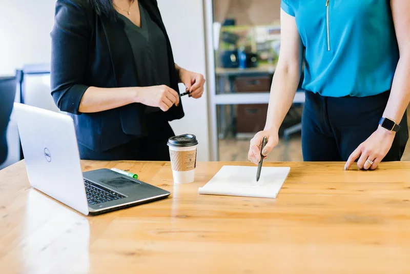 Dos personas revisando documentos y tomando notas en una mesa de trabajo con un portátil