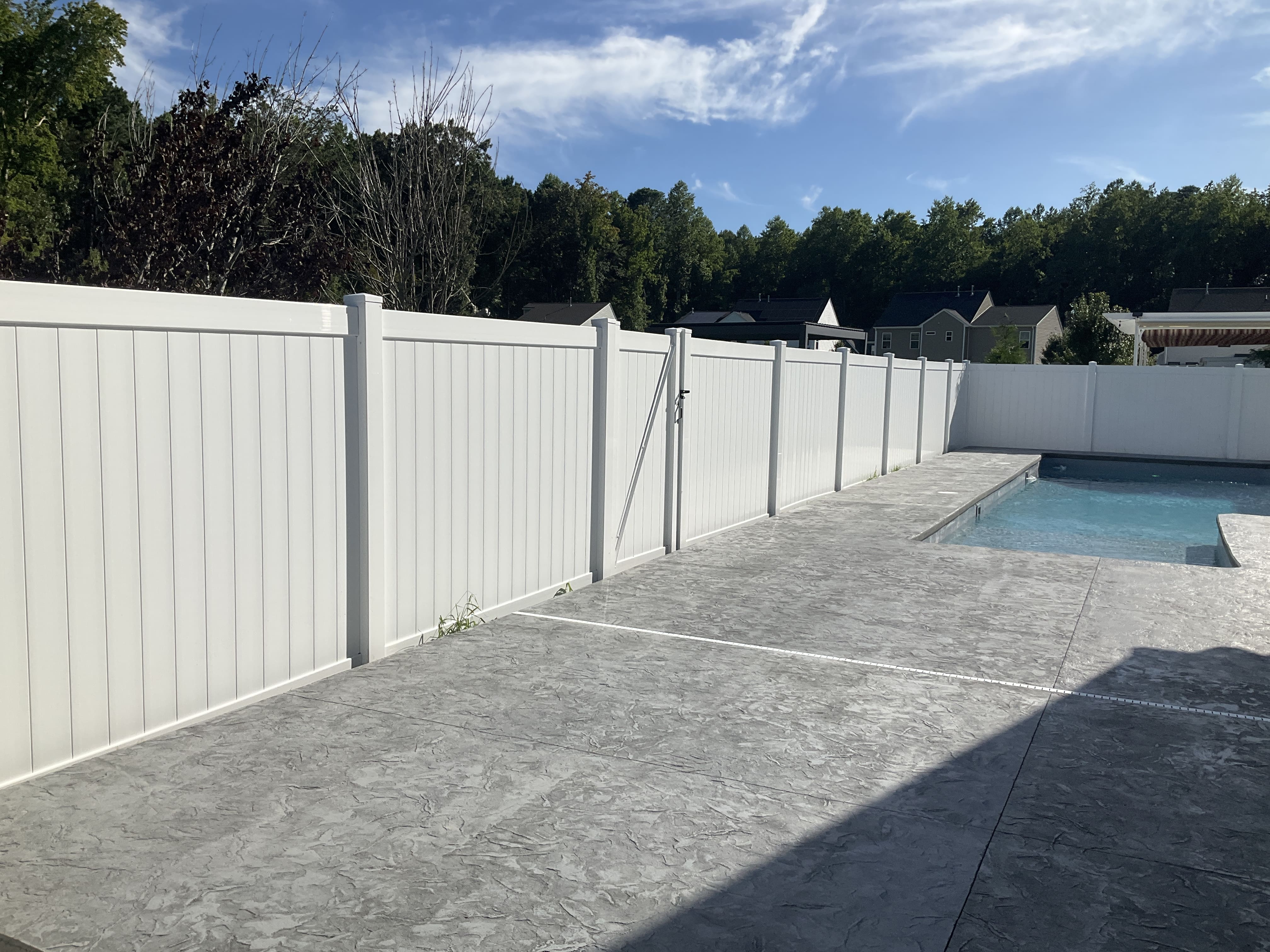 White vinyl privacy fence surrounding a pool area with textured concrete decking and a clear blue sky above.