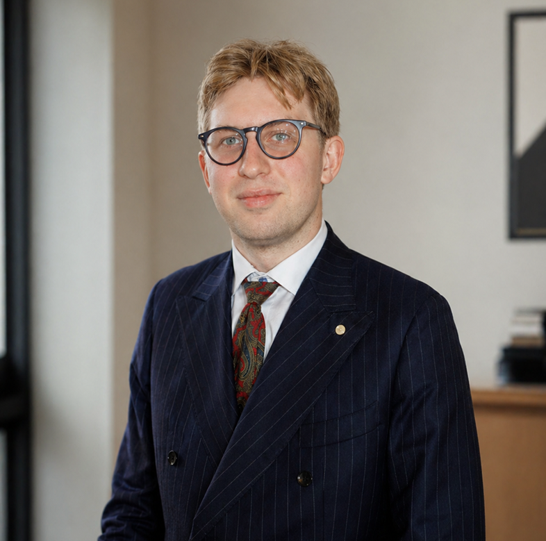 Mand med briller iført mørkeblå pinstripe jakkesæt og mønstret slips i et formelt miljø.