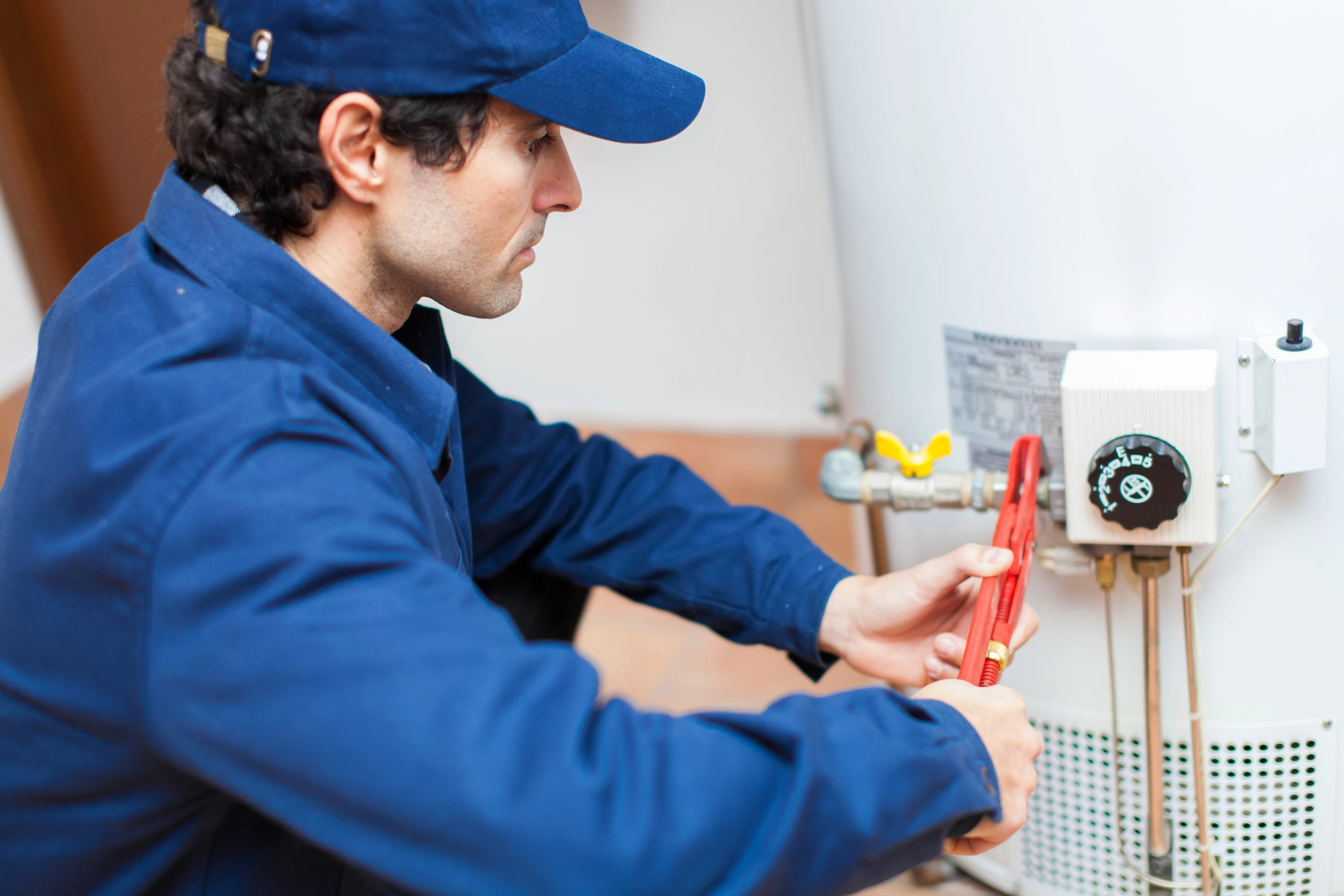 A man in a blue jacket repairs a water heater.