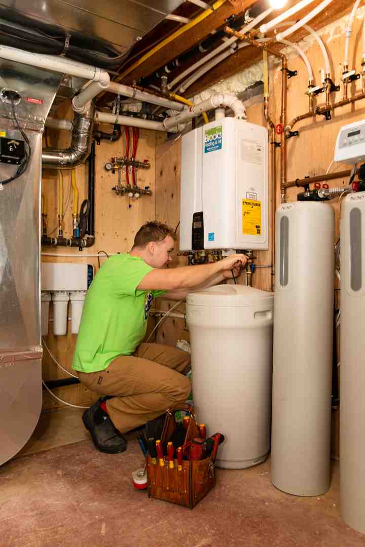 A Brooks Heating and Air technician carefully working on the plumbing connections of a tankless water heater, ensuring secure and leak-free installation - Install tankless water heater