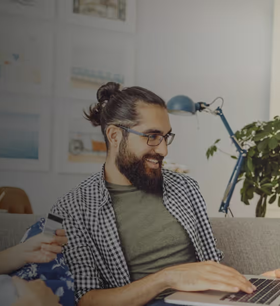 Smiling bearded man working on laptop with desk lamp and plant nearby