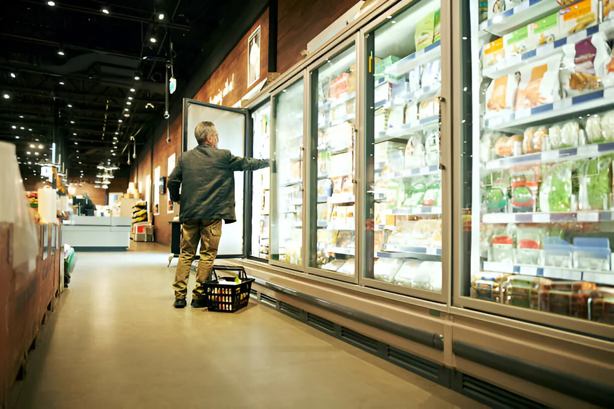 Shopper browsing frozen food section with shopping basket in grocery store