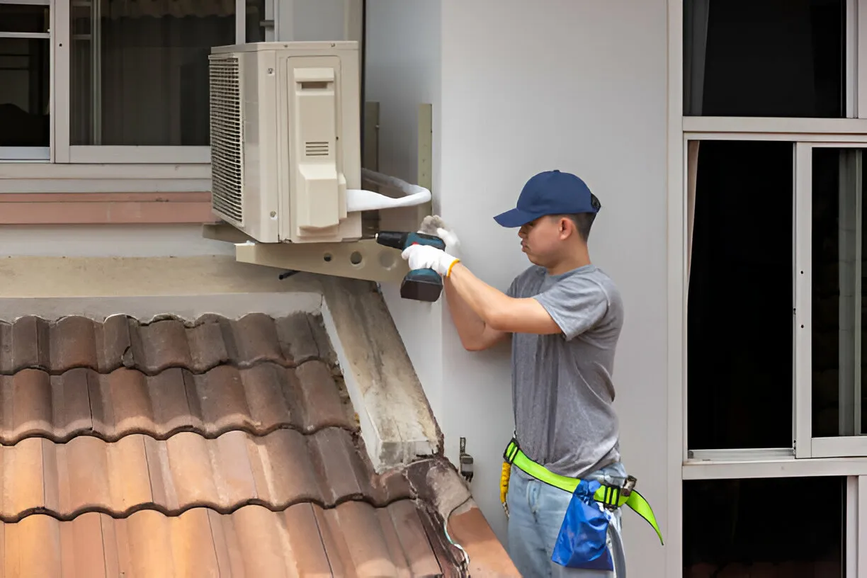 Technician installing air conditioning unit on exterior wall with roof tiles