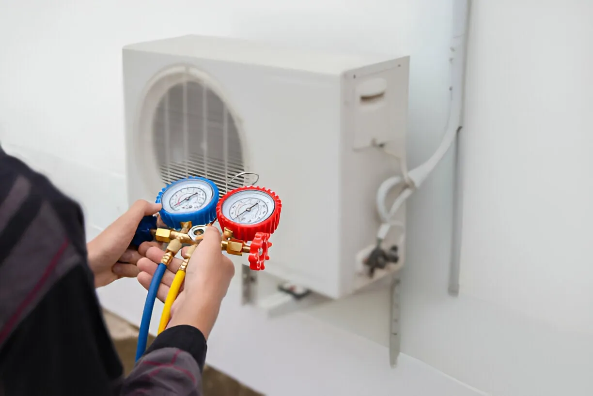 Technician checking air conditioning unit with colored pressure gauges