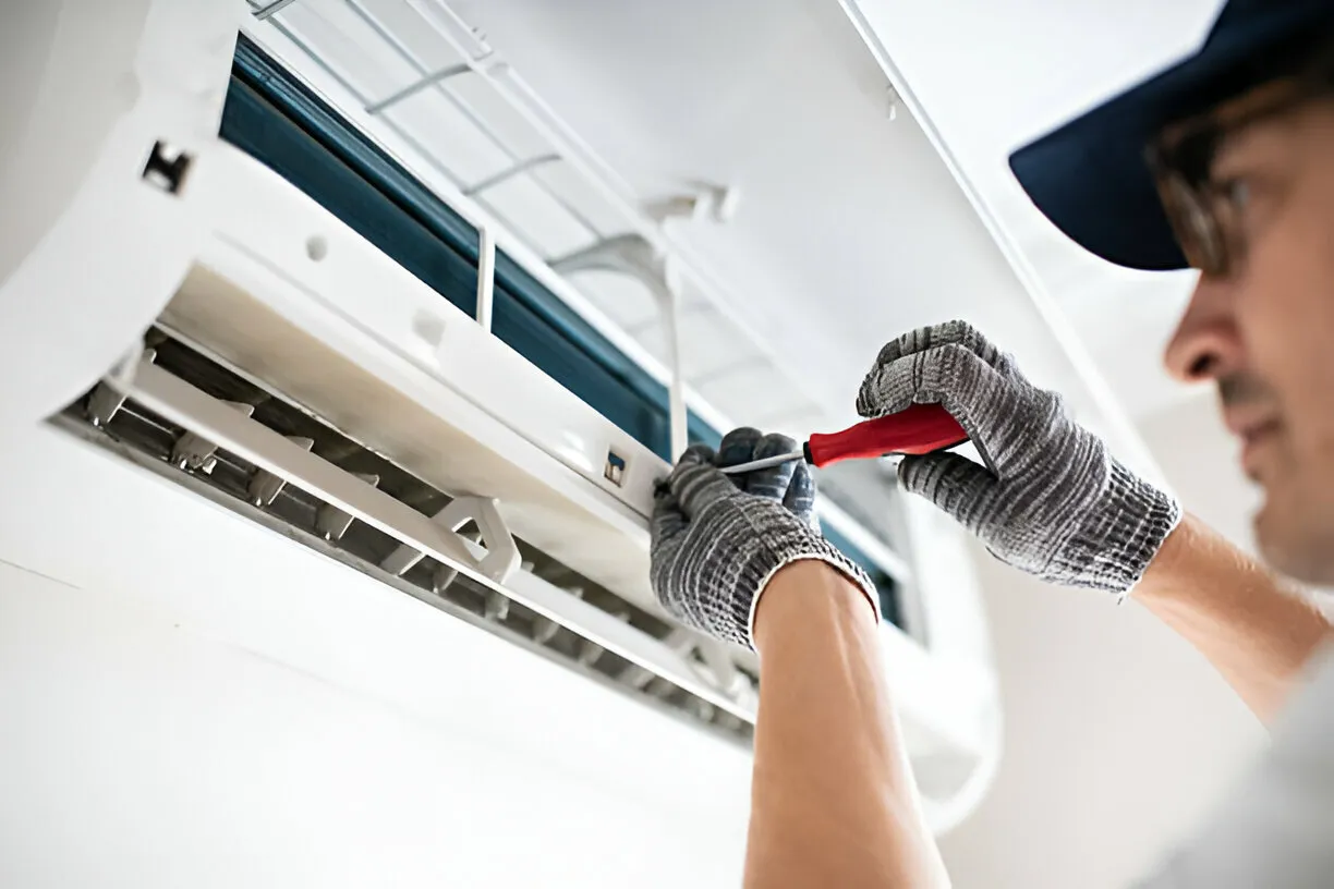 Technician repairing air conditioning unit with screwdriver and protective gloves