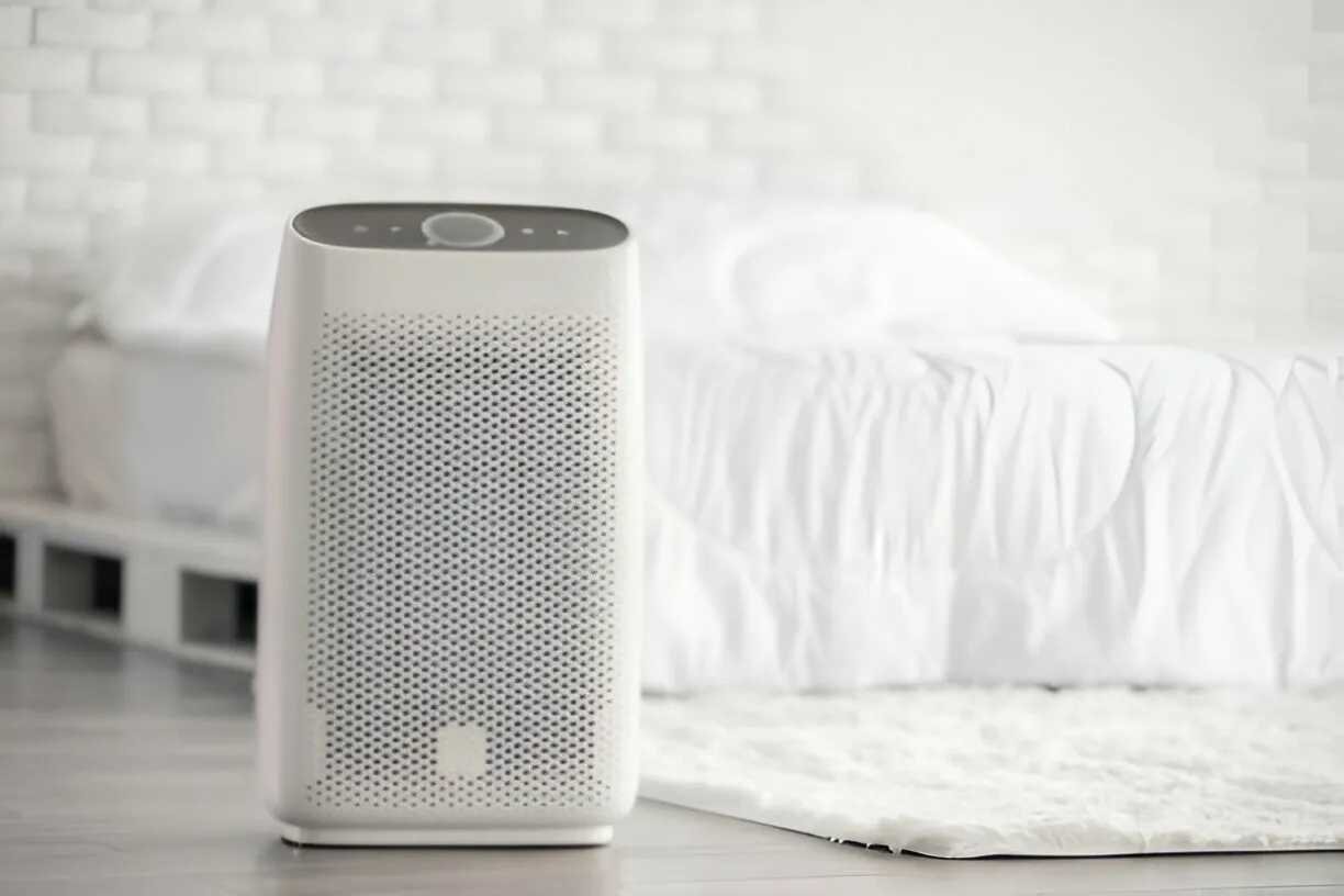 White air purifier on floor next to bed in minimalist bedroom