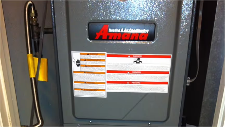Amana HVAC heating unit with instruction labels and yellow electrical conduit