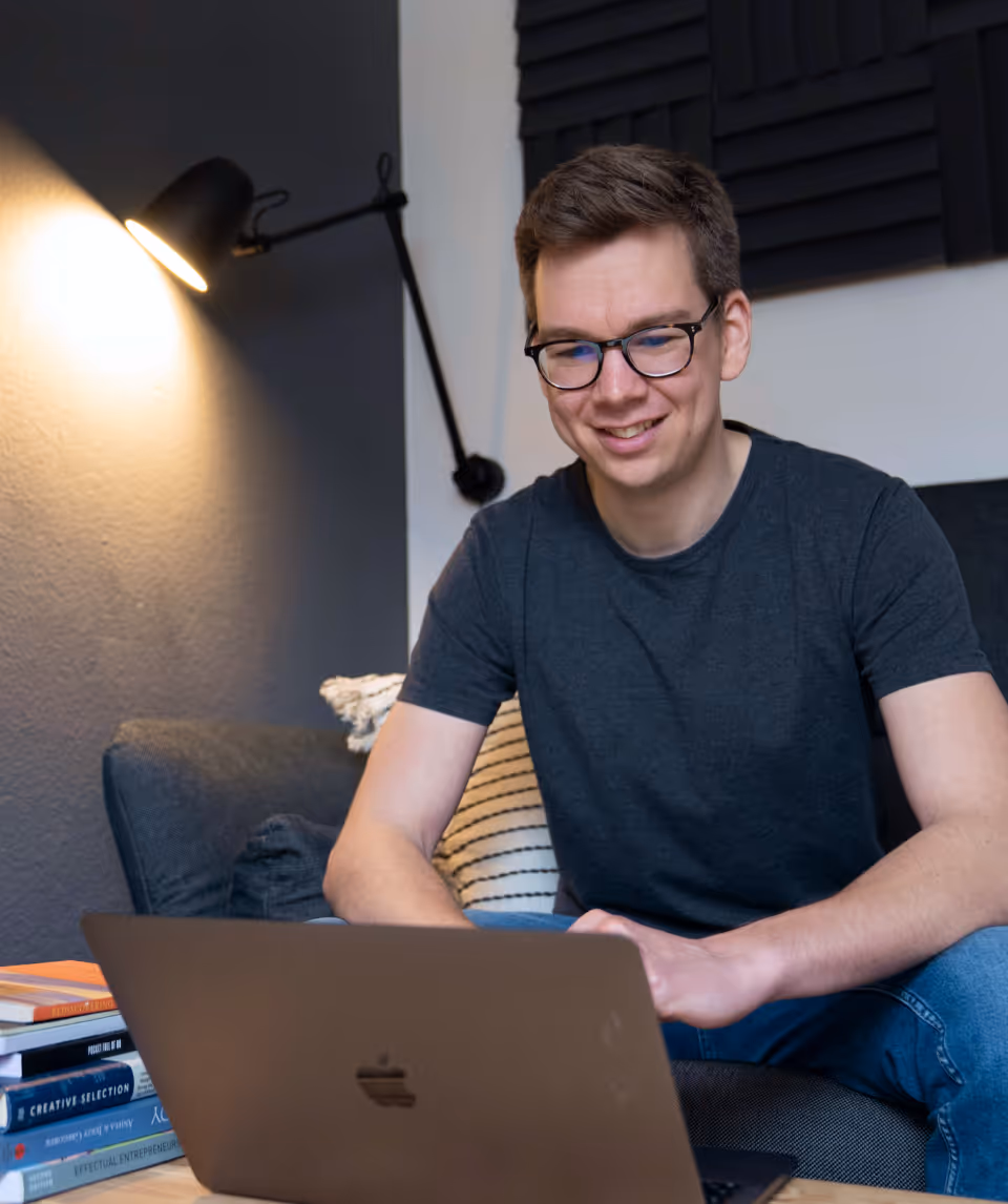 Portrait of Matthias Cordes sitting at his office couch looking at his computer.