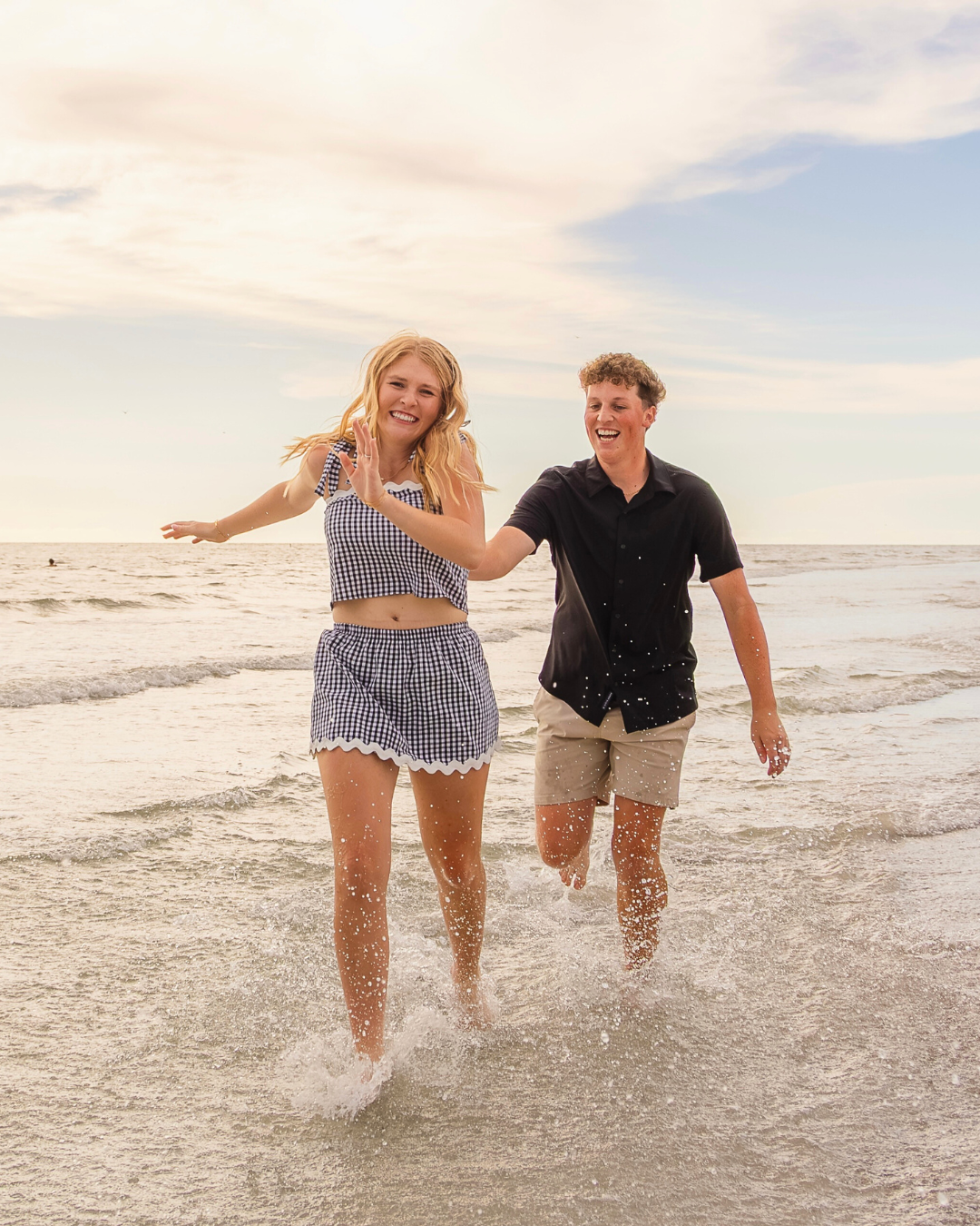Olivia and Carson laughing and running through the shallow ocean water, splashing as they go. Fun and candid lifestyle couples session.