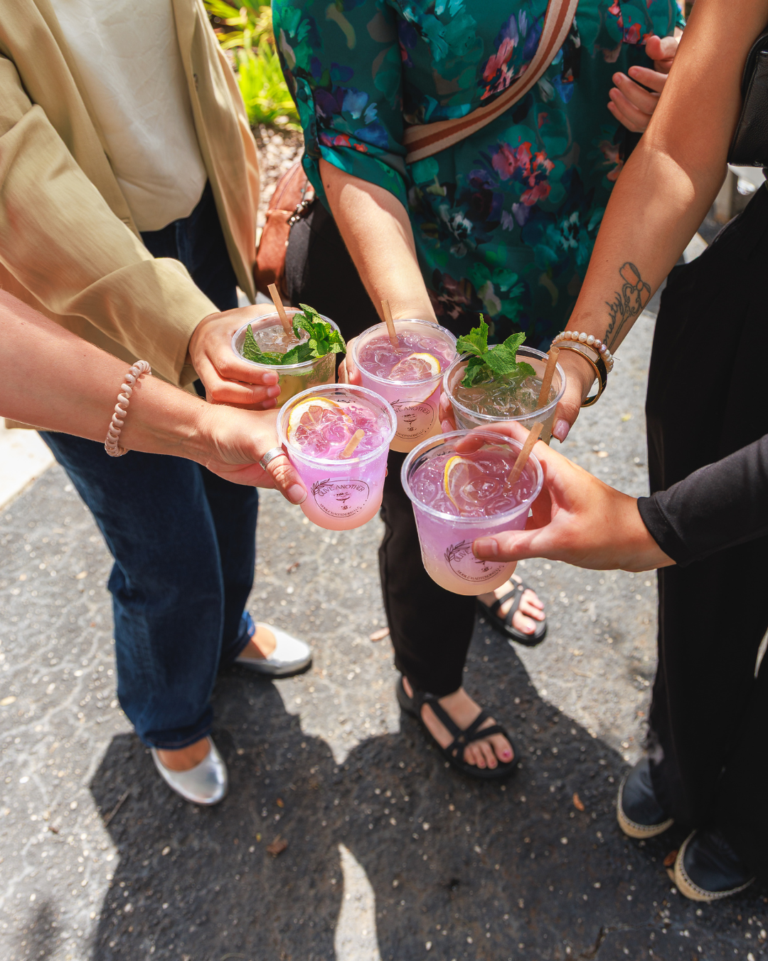 An overhead shot of multiple hands holding up colorful custom drinks in a toast, symbolizing celebration and connection at the United Women’s Network of Florida inaugural women’s networking event.