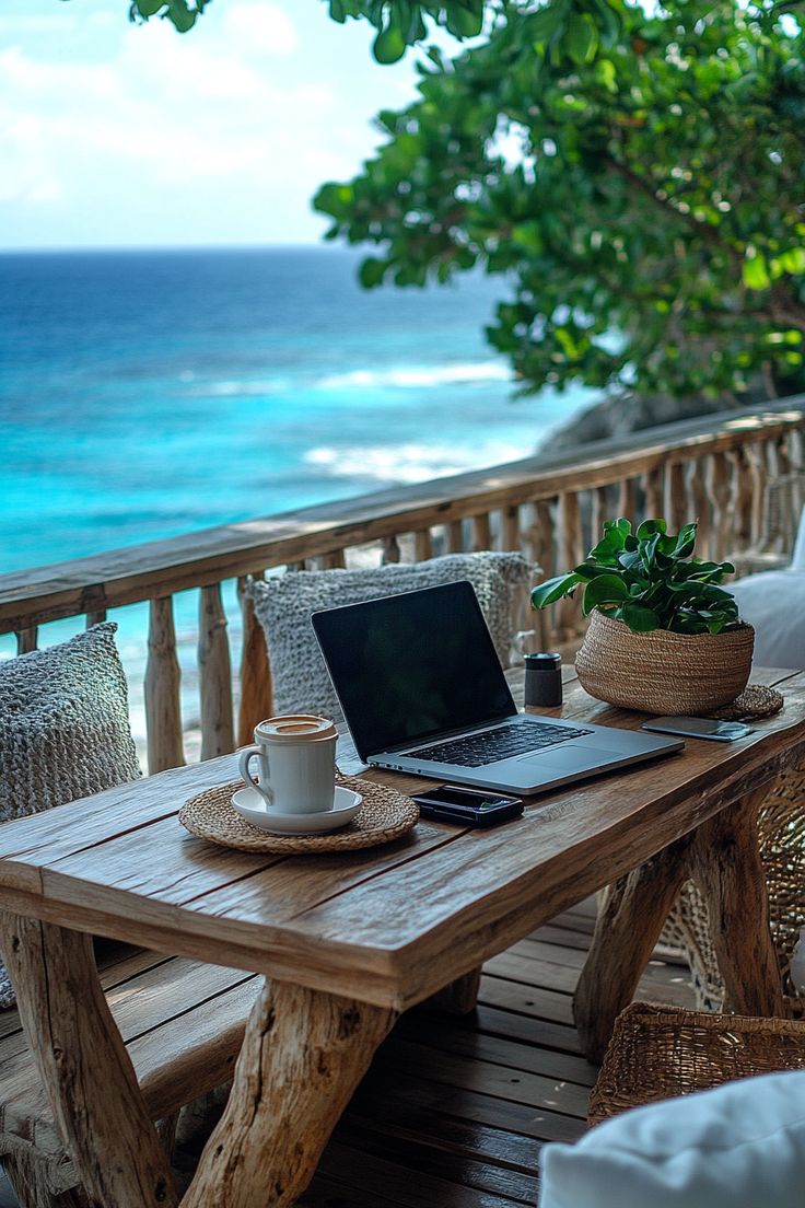 a laptop on a wooden table overlooking the ocean