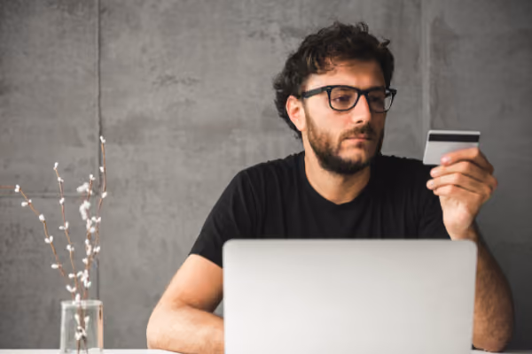 a man sitting in front of a laptop while holding a credit card in his left hand