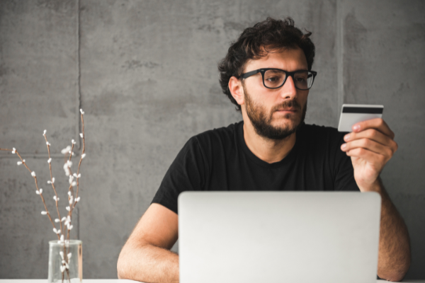 a man sitting in front of a laptop while holding a credit card in his left hand