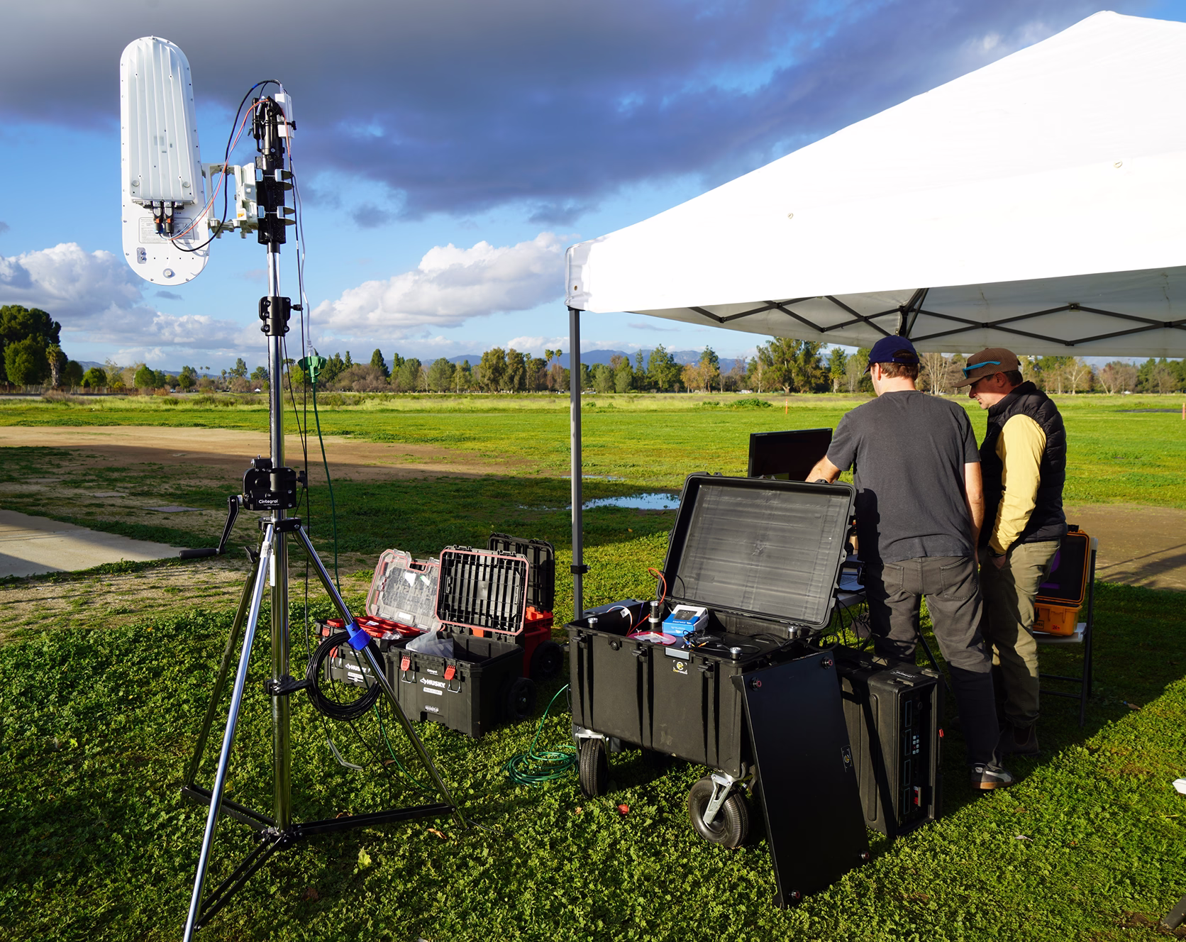 LightBridge unit on a tripod mast at an outdoor test site, with technicians setting up nearby