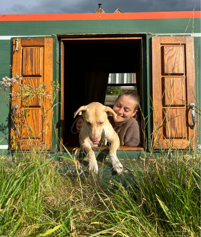 Woman and dog looking out of the hatch of a green narrowboat, smiling.