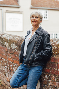 Linda Mather wearing a leather jacket and smiling while leaning against a wall