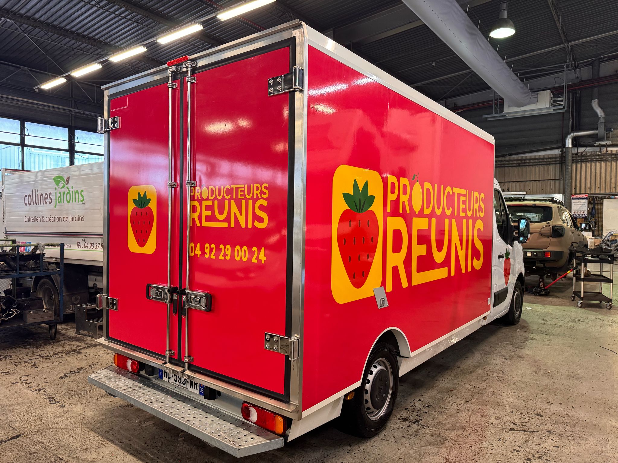Red delivery truck inside a garage with a yellow strawberry logo and the words 'Producteurs Reunis' in yellow on its side and back.
