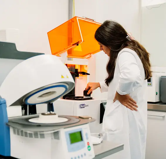 Female scientist in white lab coat operating lab equipment in a bright laboratory.