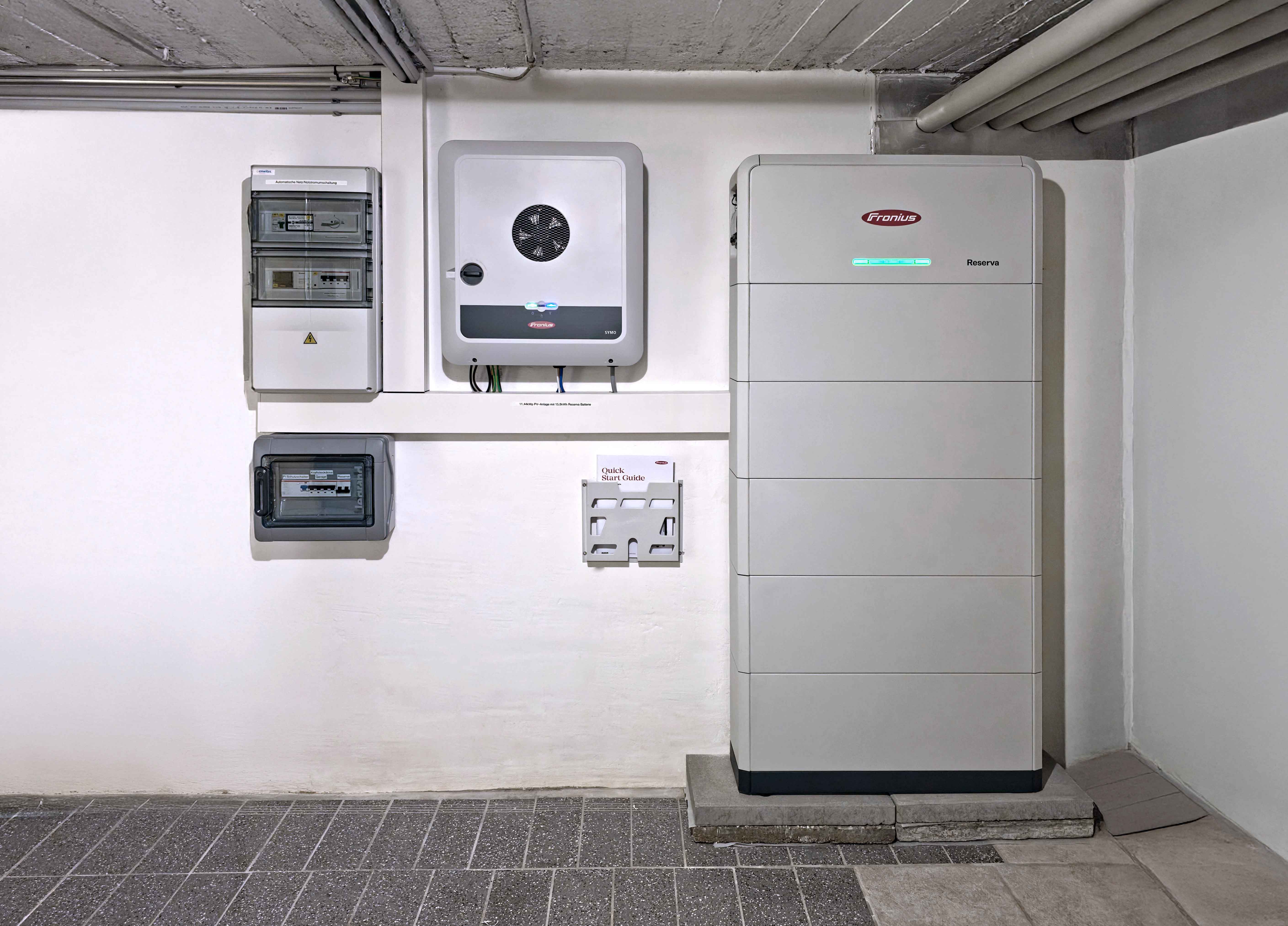 Moderne Fronius Solarspeicheranlage in einem Keller mit Steuergerät, Sicherungskasten und Schnellstartanleitung an der Wand montiert.