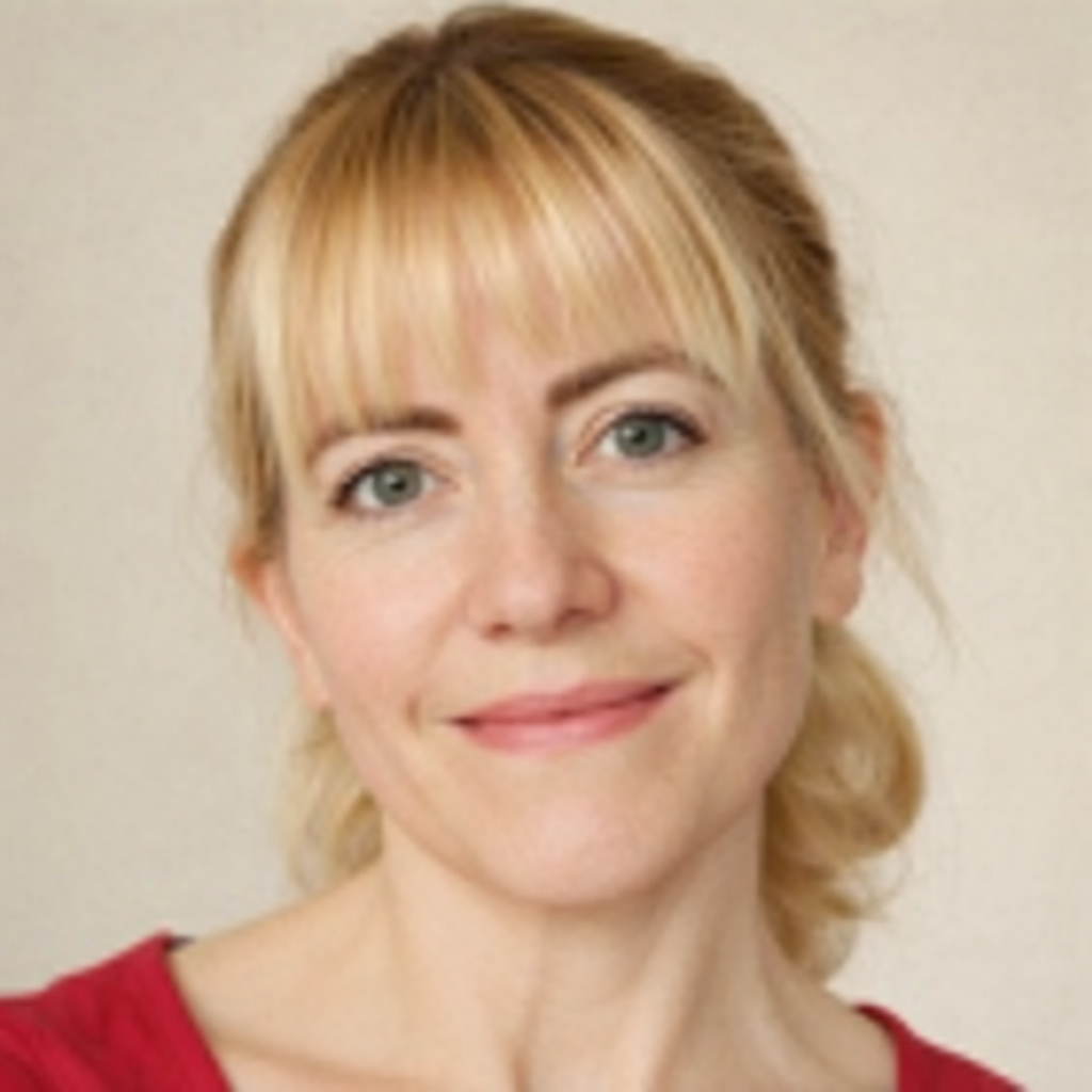 Blondýna se zelenýma očima a ofinou, usmívající se do kamery v červeném tričku.