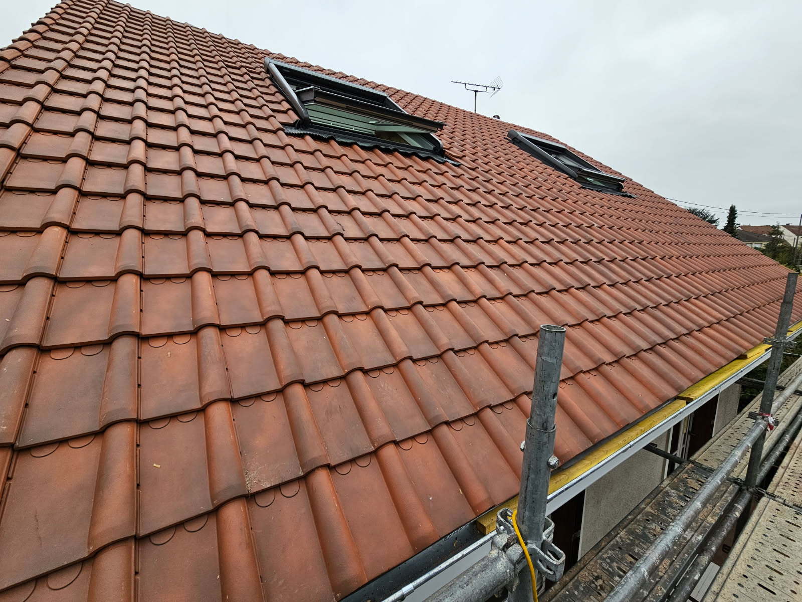 Toit en tuiles rouges avec deux fenêtres de toit ouvertes et échafaudage au premier plan.