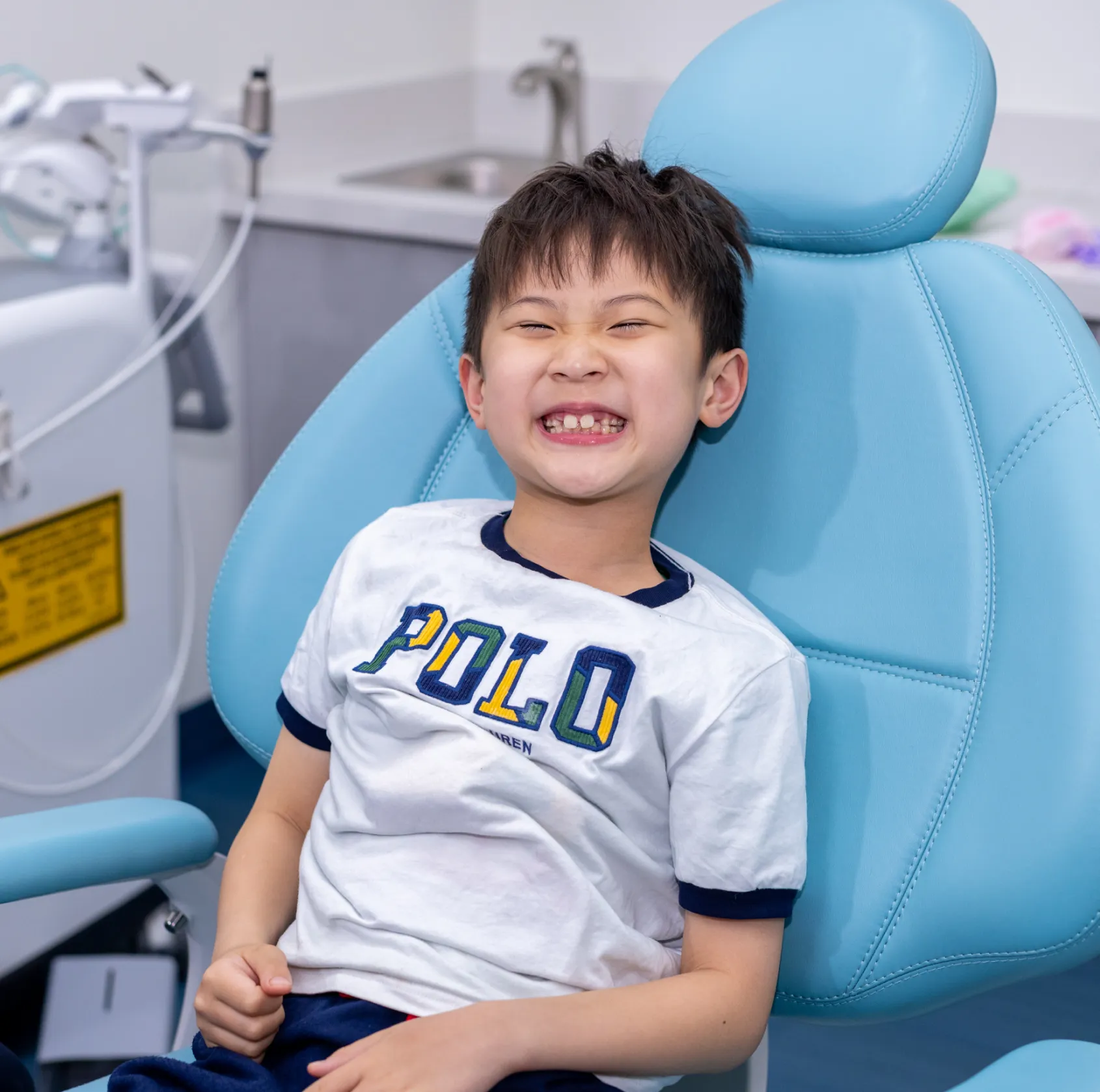 Smiling young boy sitting in a blue dental chair in a dental clinic.