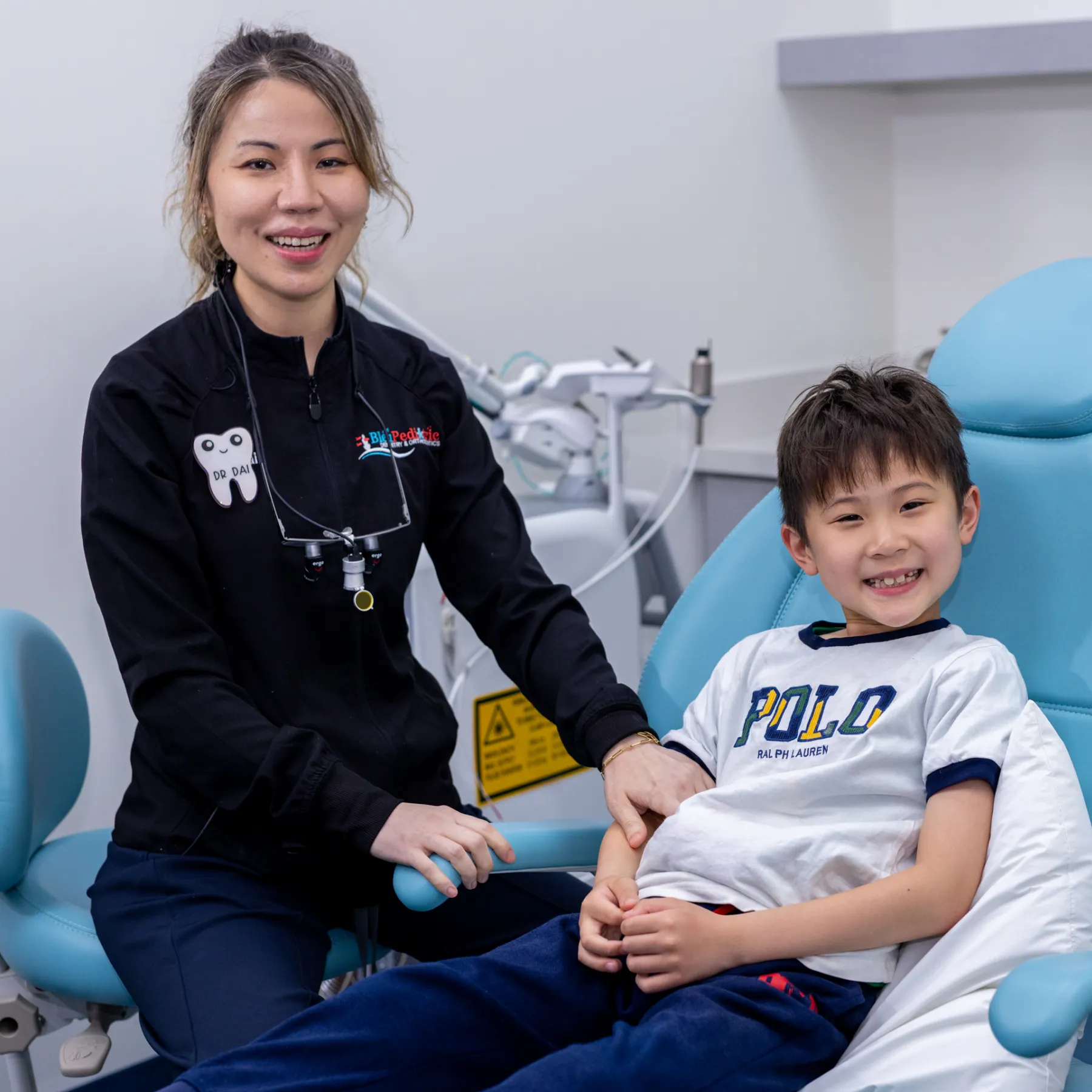 Female dentist smiling next to a happy young boy sitting in a dental chair.