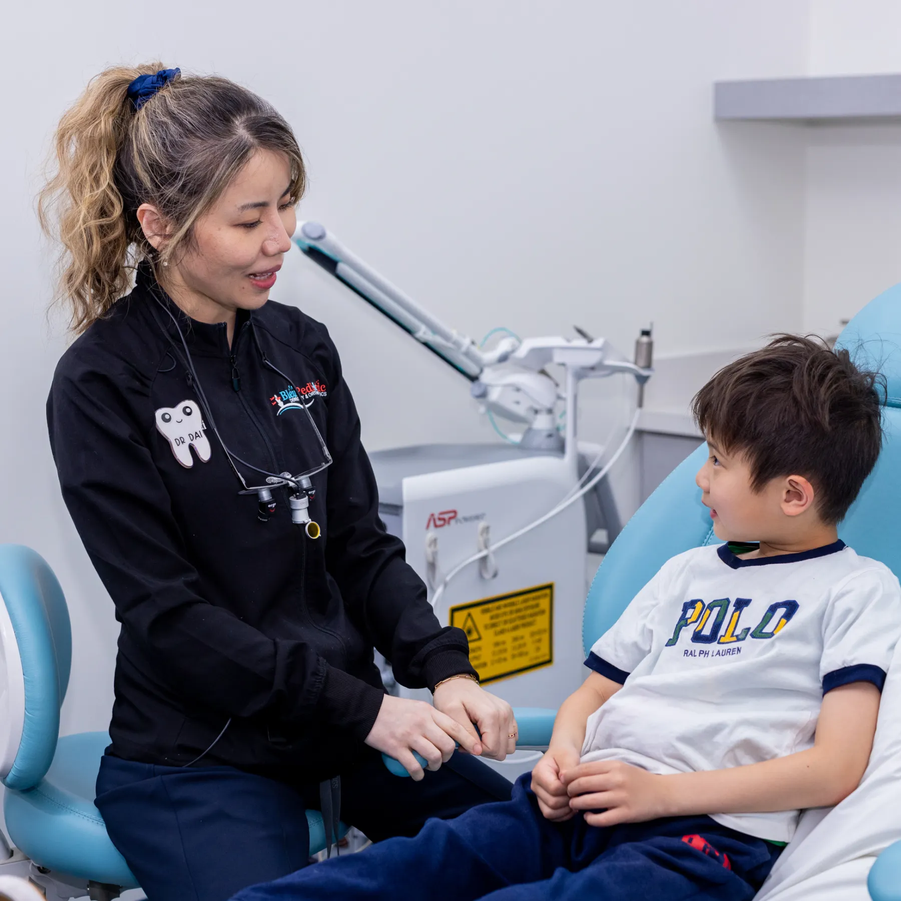Female dentist talking to a young boy sitting in a dental chair in a clinic.