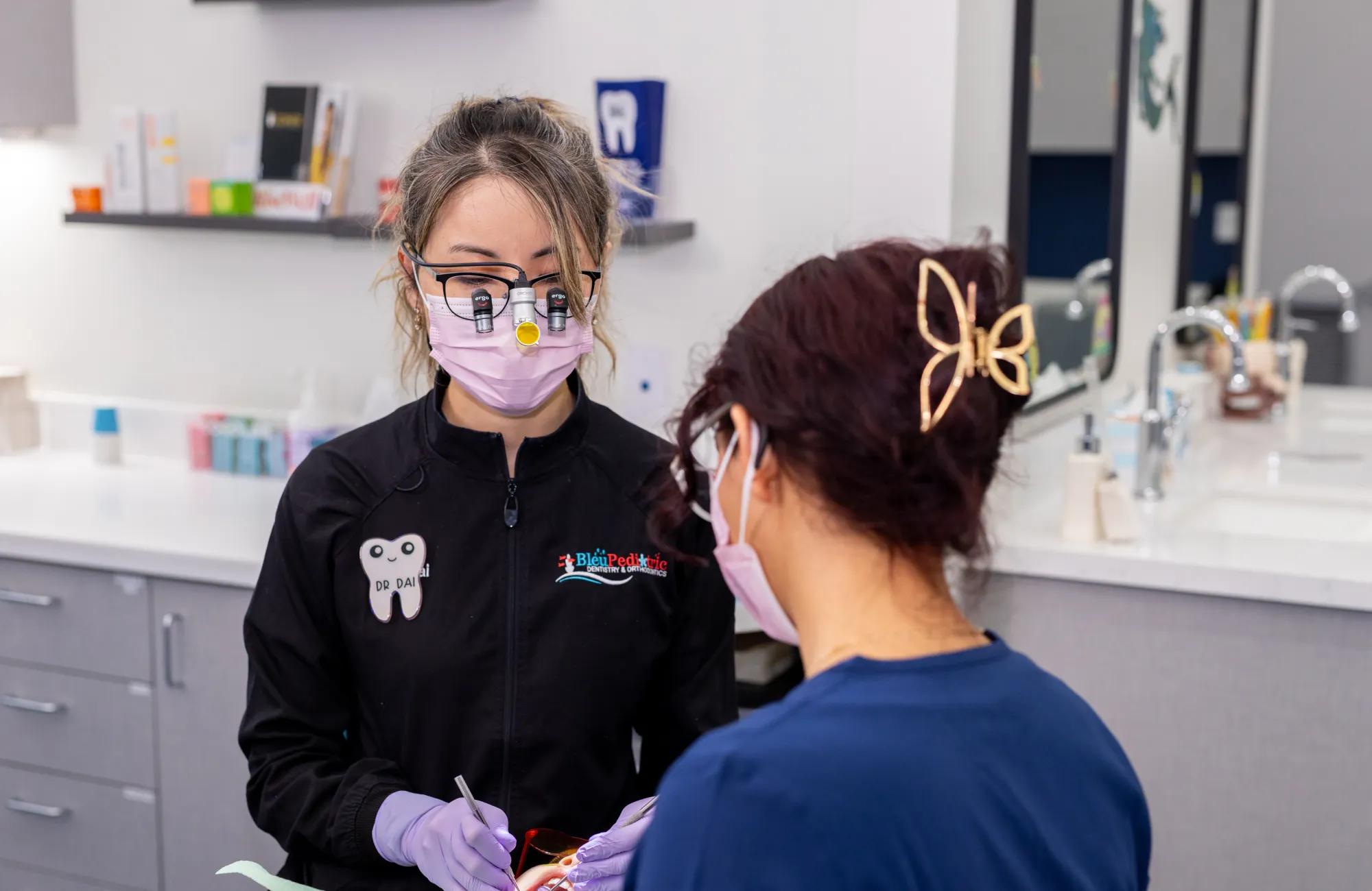 Female dentist in a mask and magnifying glasses examining a patient in a dental clinic.