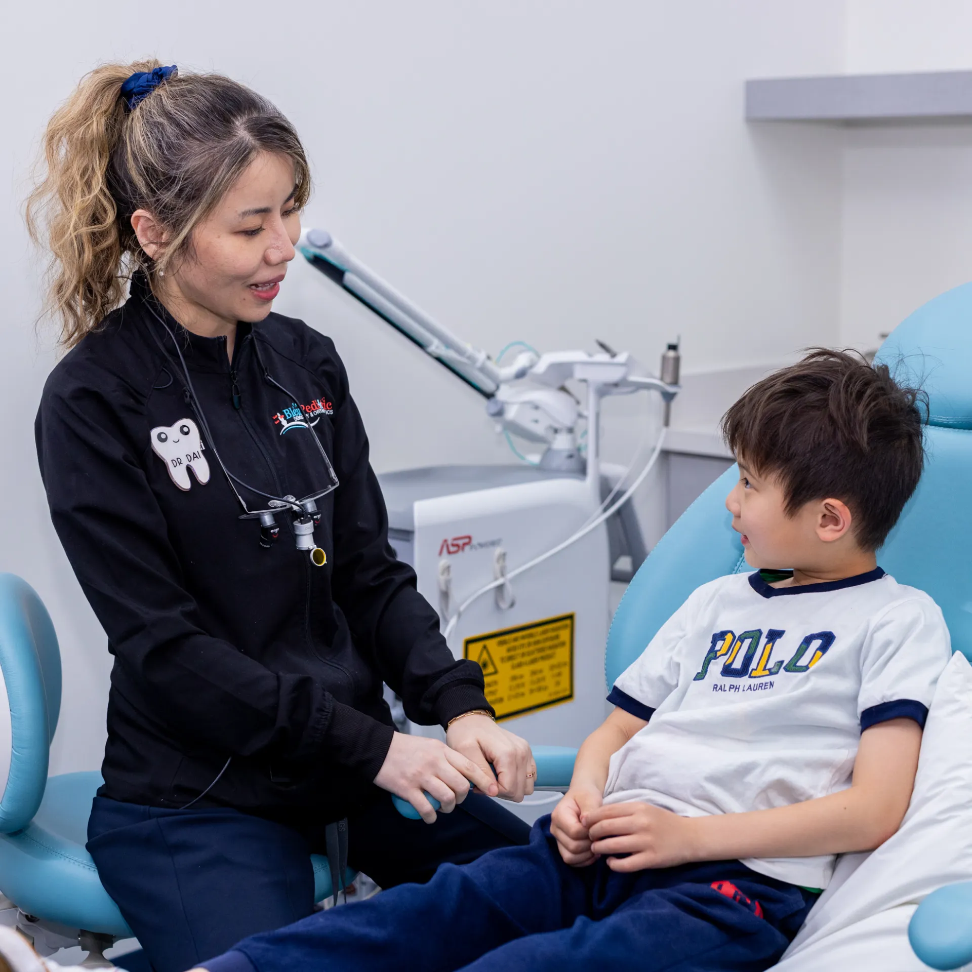 Female dentist talking to a young boy seated in a dental chair in a clinic.