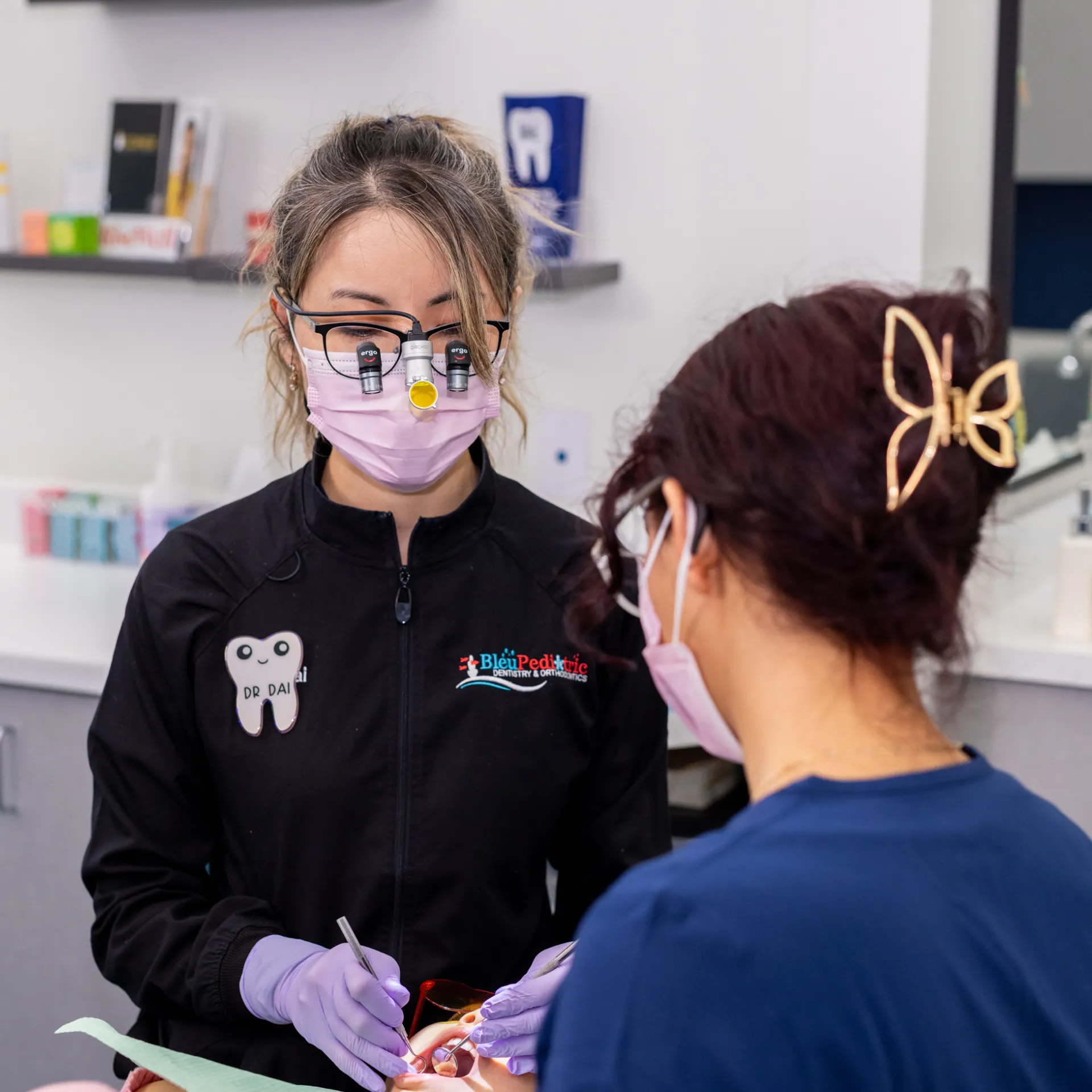 Dentist wearing magnifying glasses and a mask treats a patient in a dental clinic.