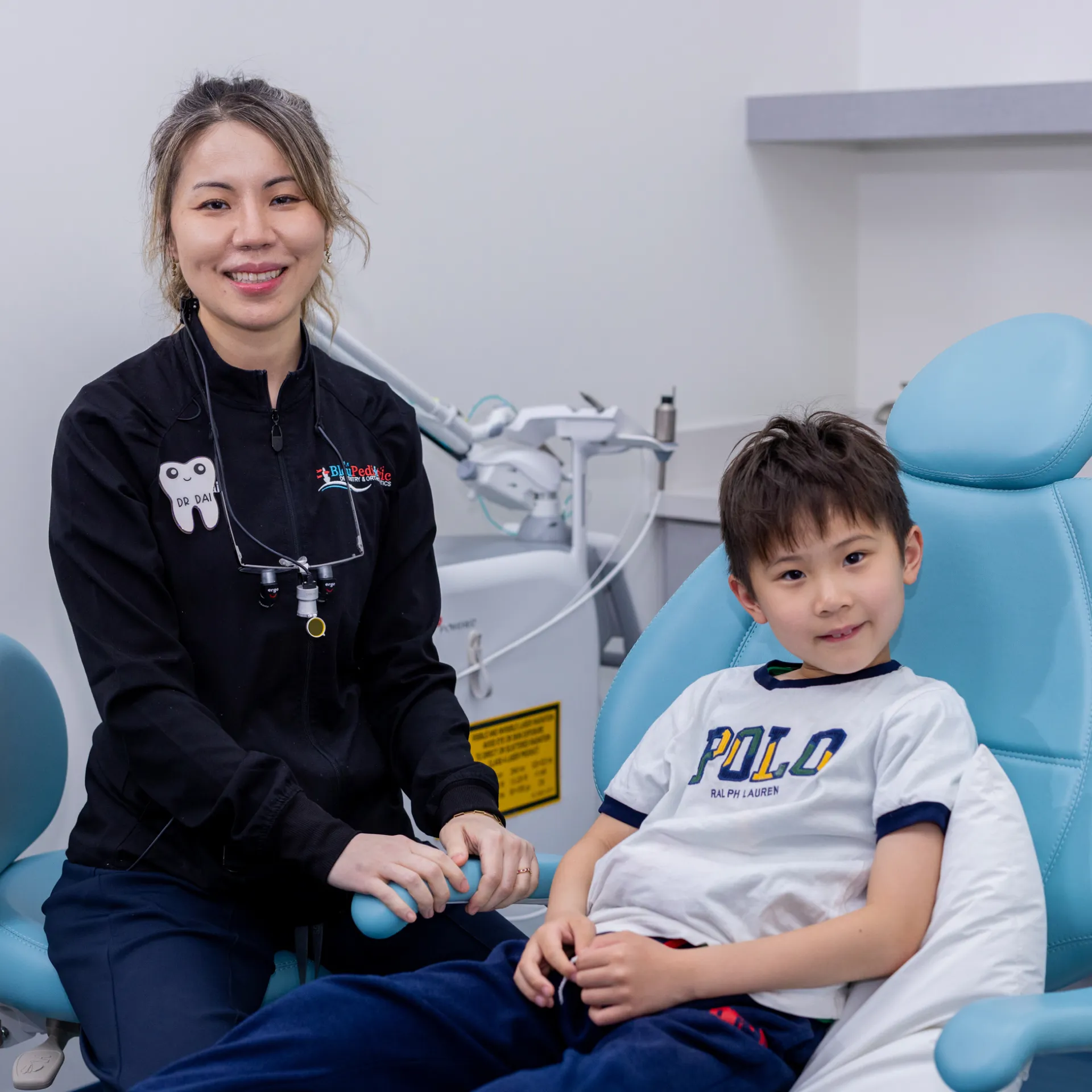Female dentist smiling next to a young boy sitting in a dental chair in a clinic.