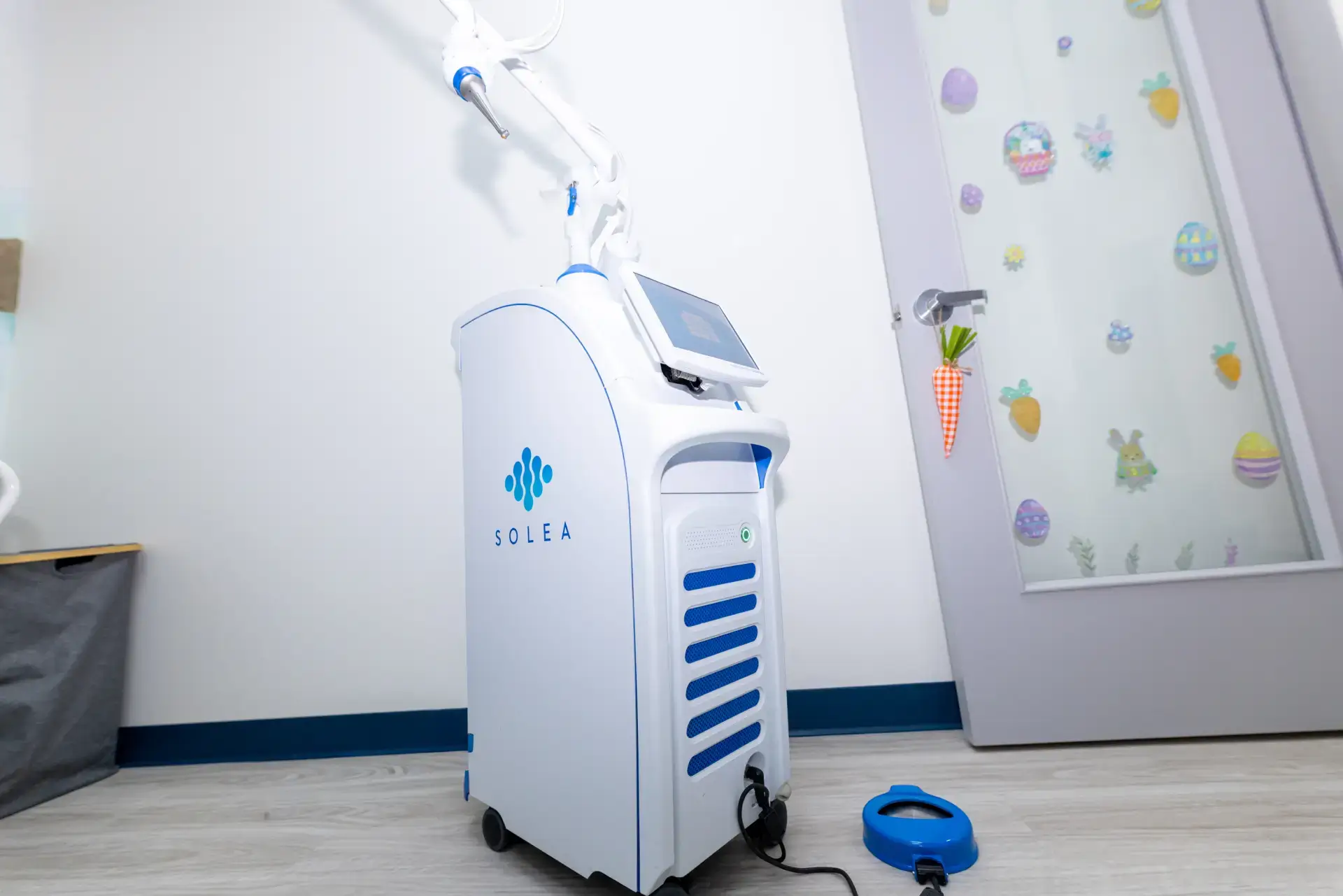 Solea dental laser machine with a touch screen in a pediatric dental office near a door decorated with Easter-themed stickers and a carrot-shaped door hanger.