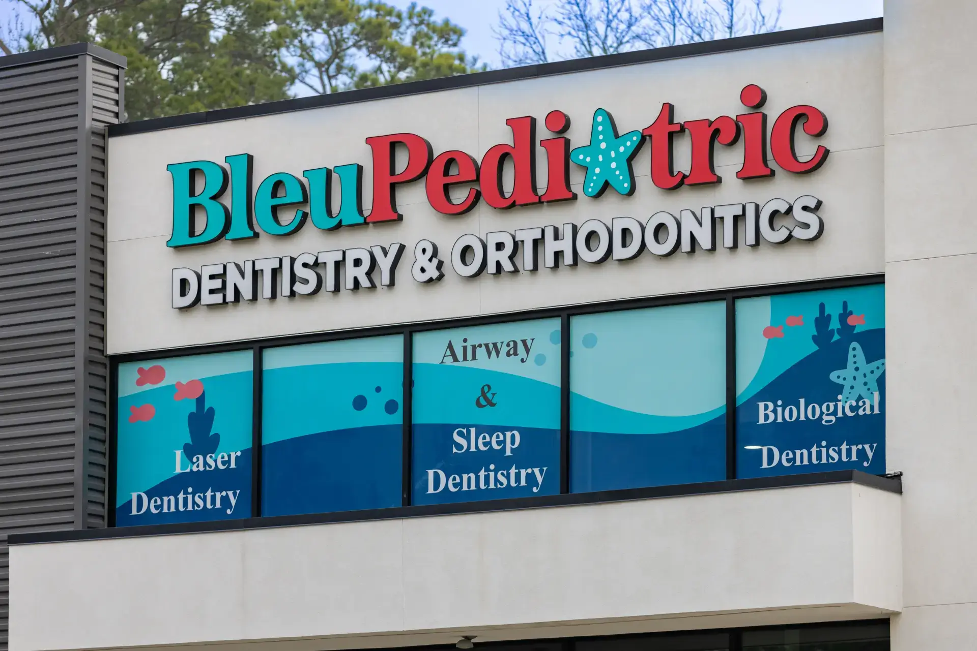 Exterior sign of Bleu Pediatric Dentistry & Orthodontics with window panels advertising Laser Dentistry, Airway & Sleep Dentistry, and Biological Dentistry.