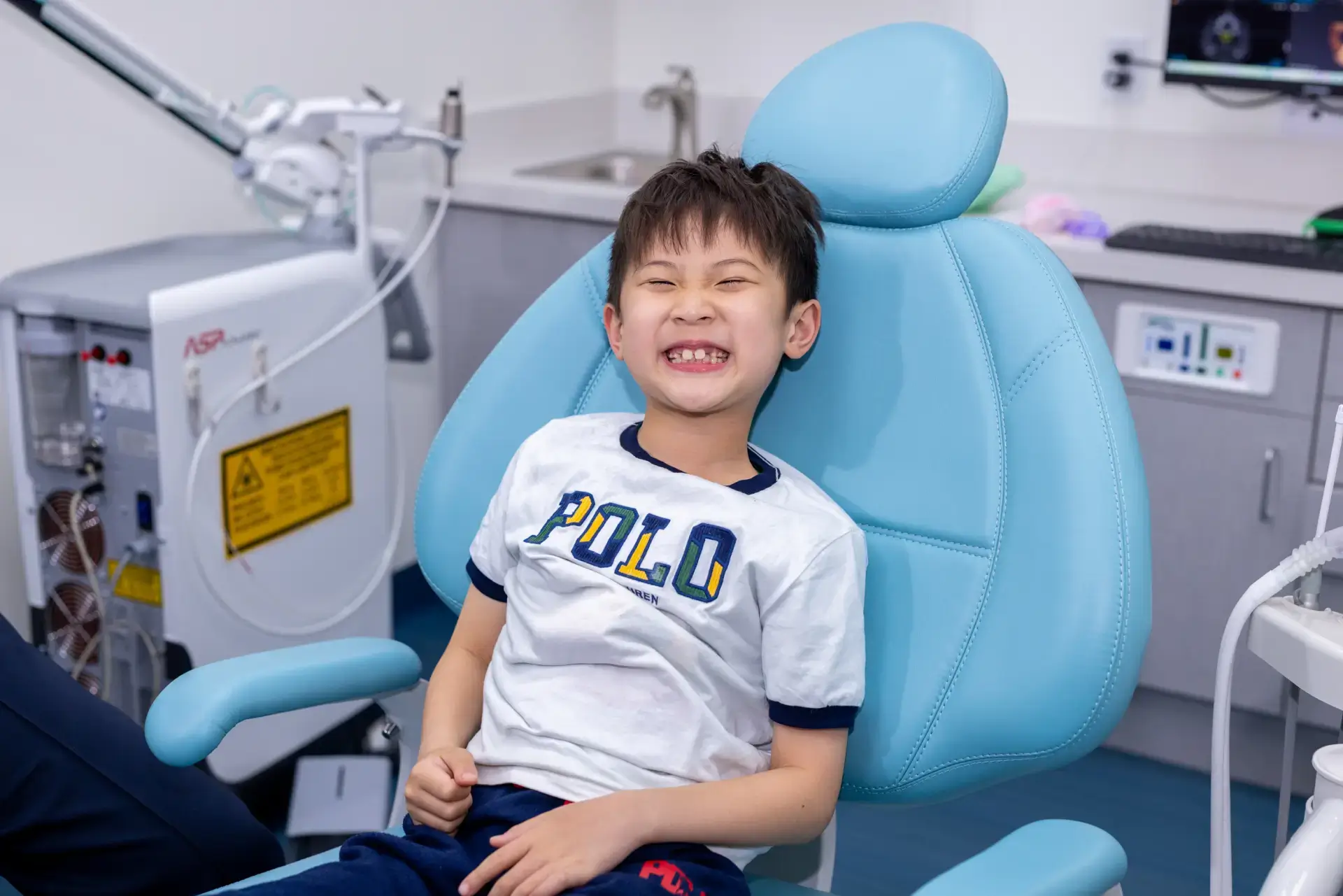 Smiling young boy sitting in a light blue dental chair in a dental clinic.