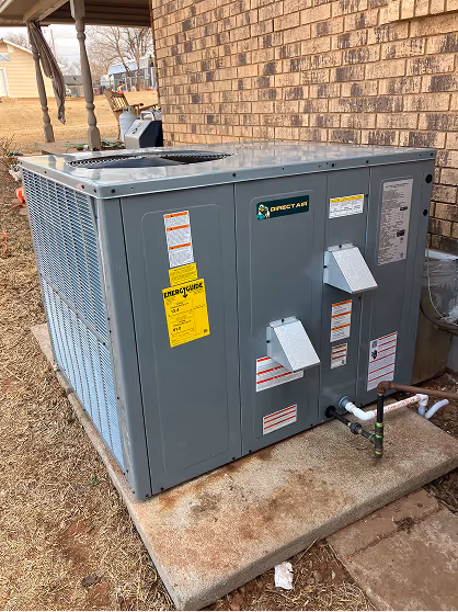 Large gray air conditioning unit installed beside brick house exterior