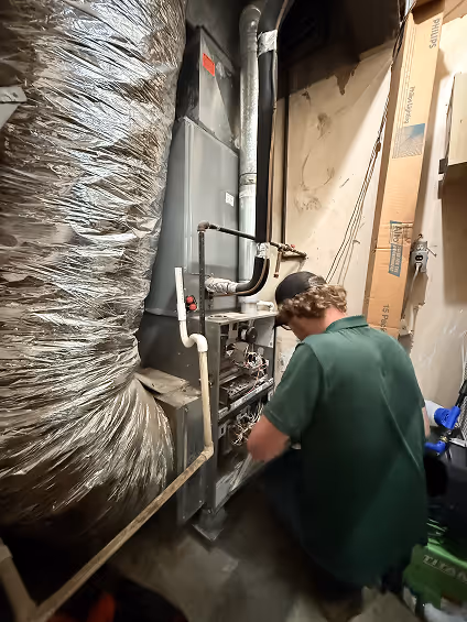 Technician in green shirt working on large industrial HVAC system with insulated ductwork