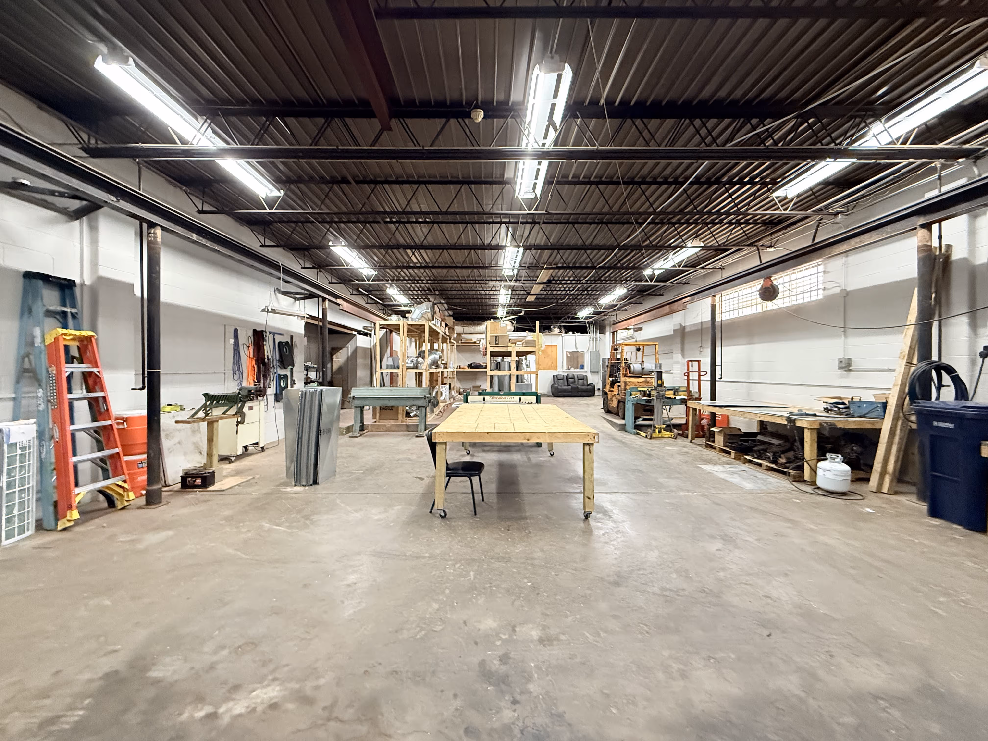 Industrial workshop with workbenches, tools, ladders, and exposed ceiling