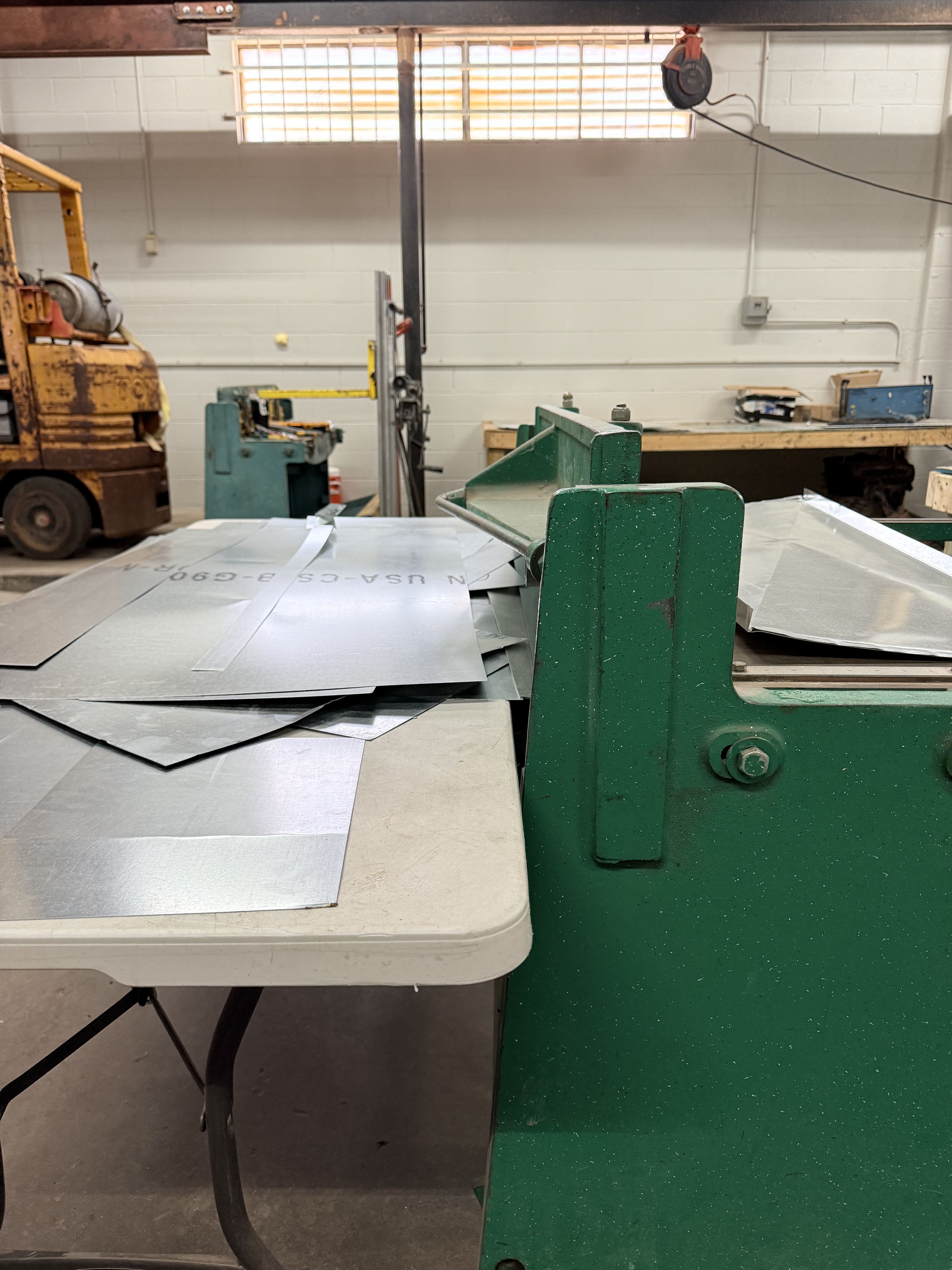 Industrial workshop with green machine, metal sheets, and yellow forklift