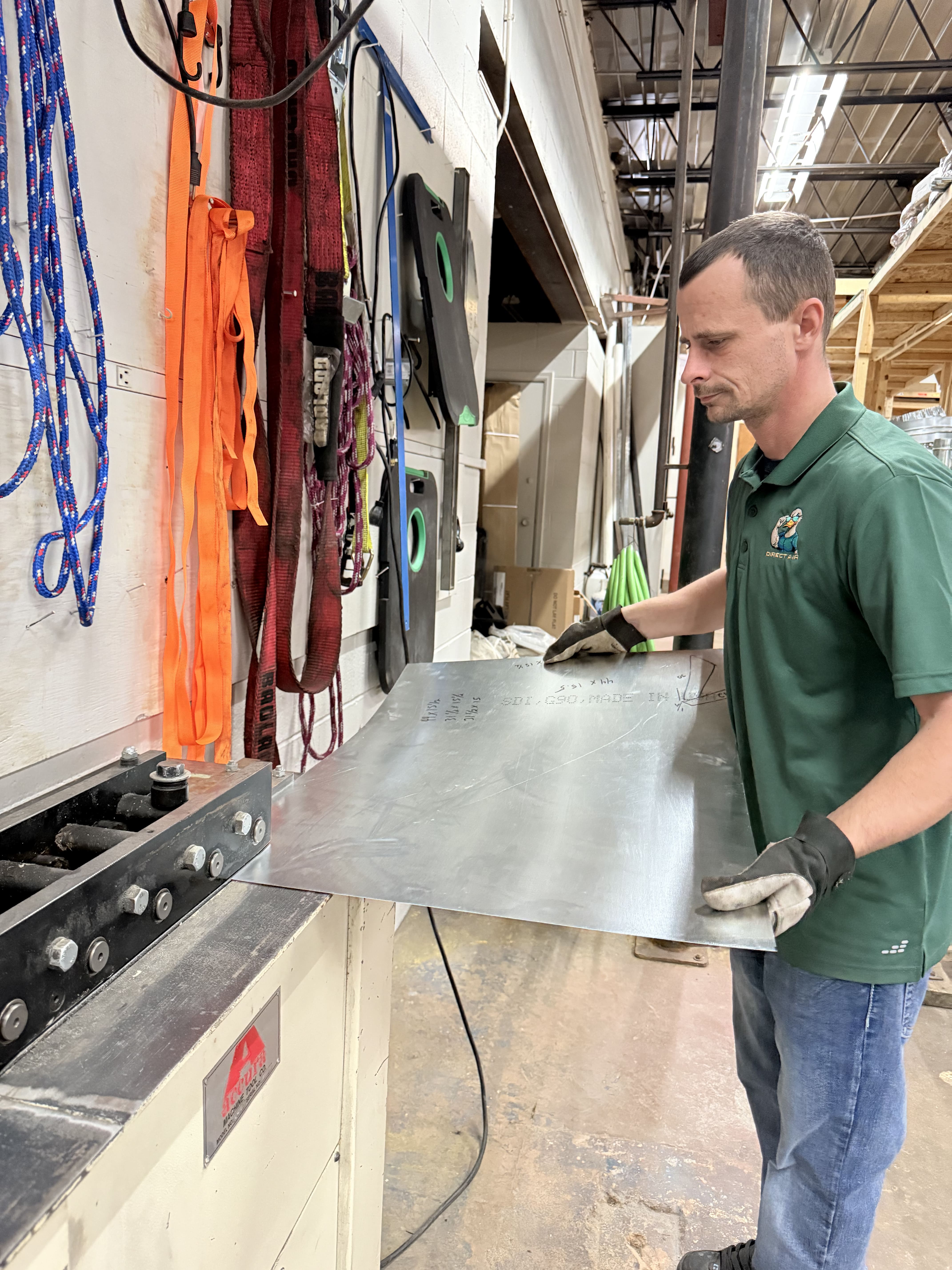 Worker handling metal sheet near colorful ropes in industrial workshop