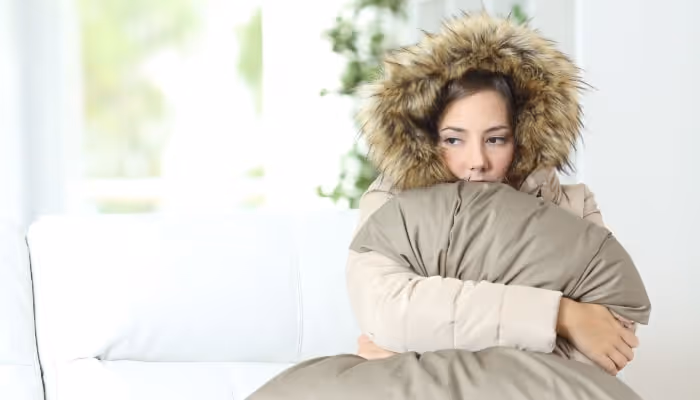 Person in warm winter coat hugging pillow, looking contemplative by window