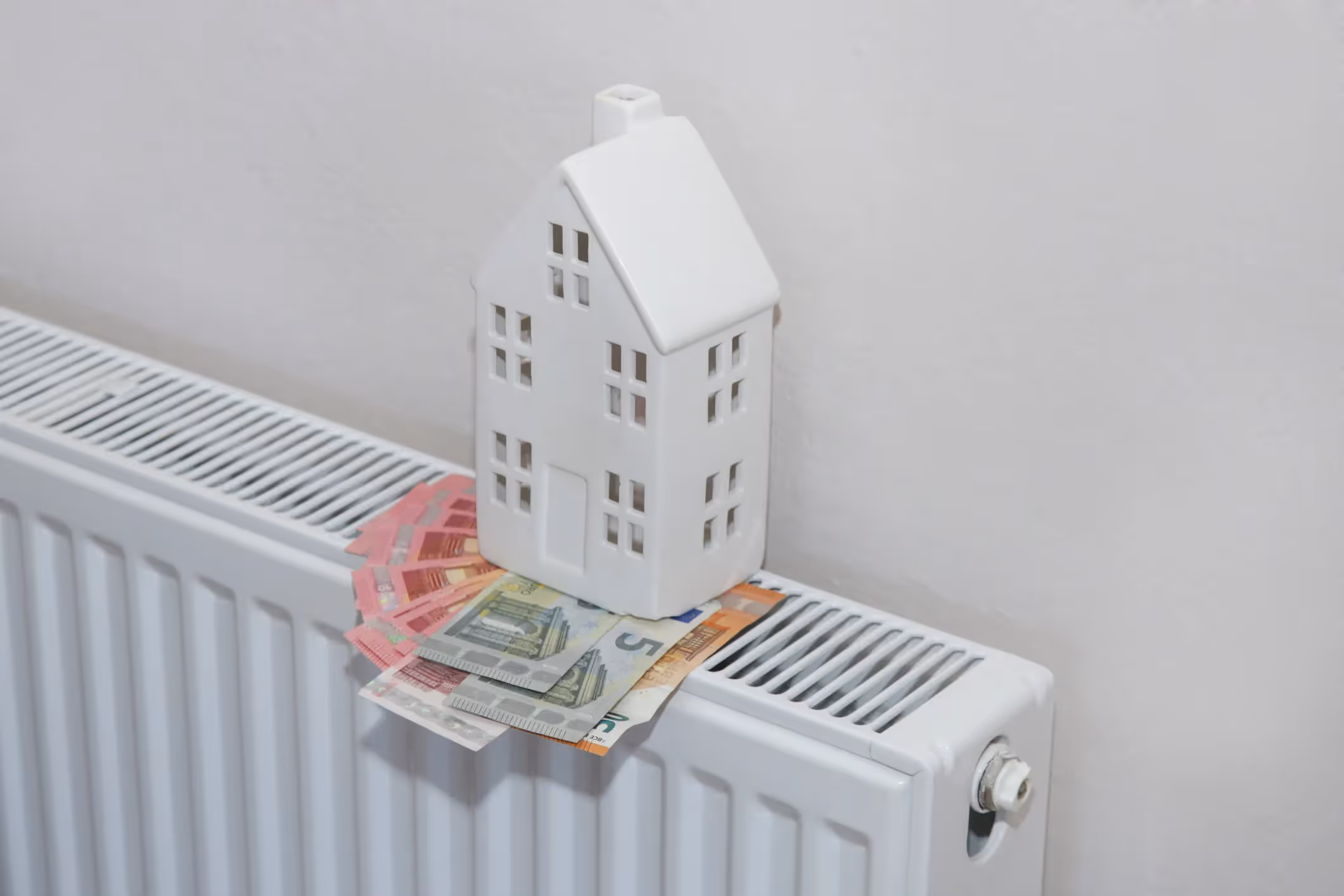 White model house on radiator with Euro banknotes, representing heating costs