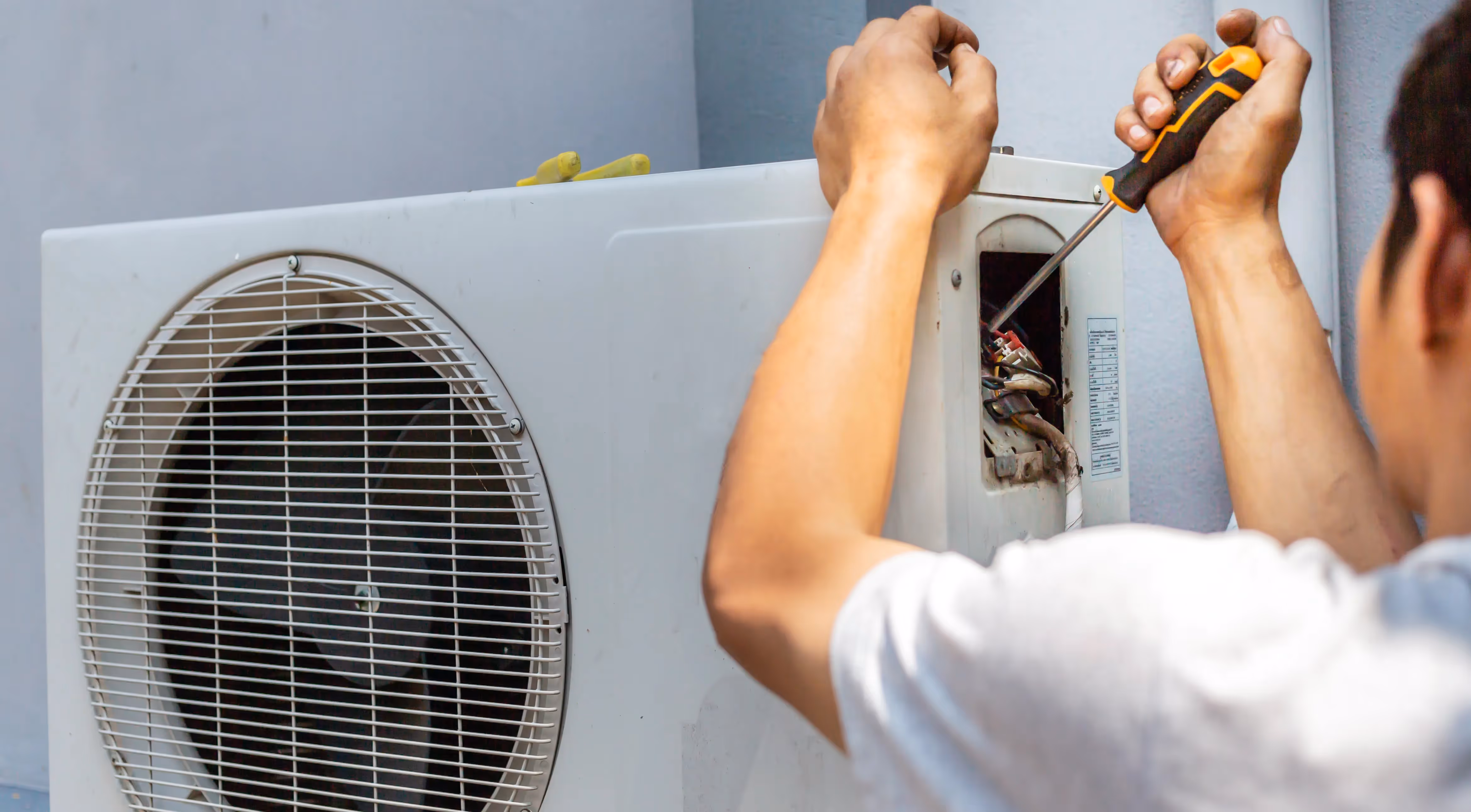 Technician repairing air conditioning unit with screwdriver
