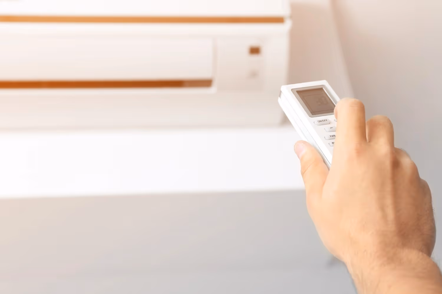 Hand holding white remote control near air conditioning unit
