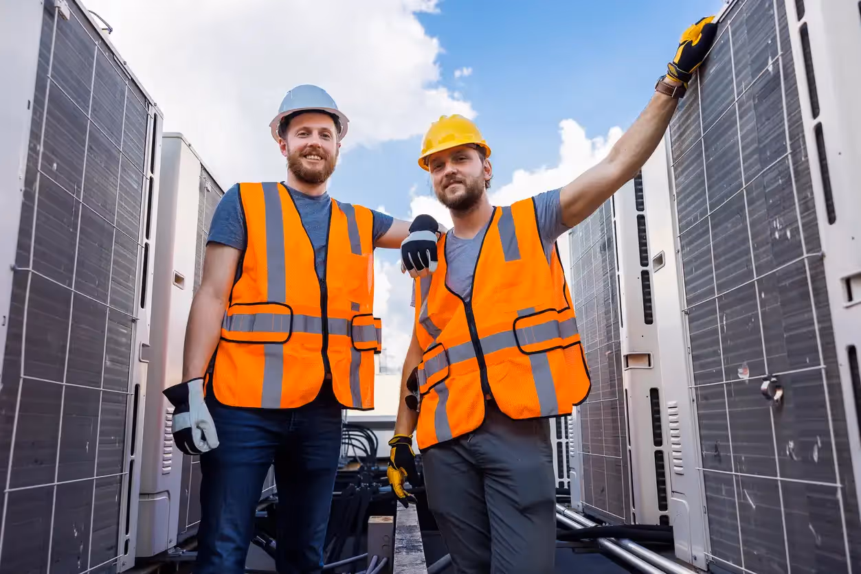 Two construction workers in safety vests and helmets standing between solar panels