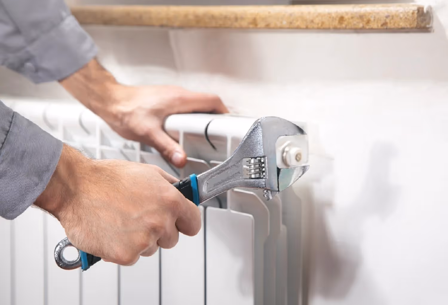 Hands using adjustable wrench to repair or tighten radiator heating element
