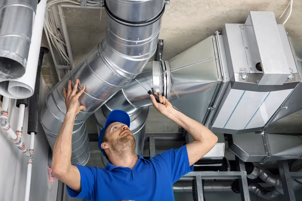 Technician in blue checking industrial ventilation ductwork and equipment